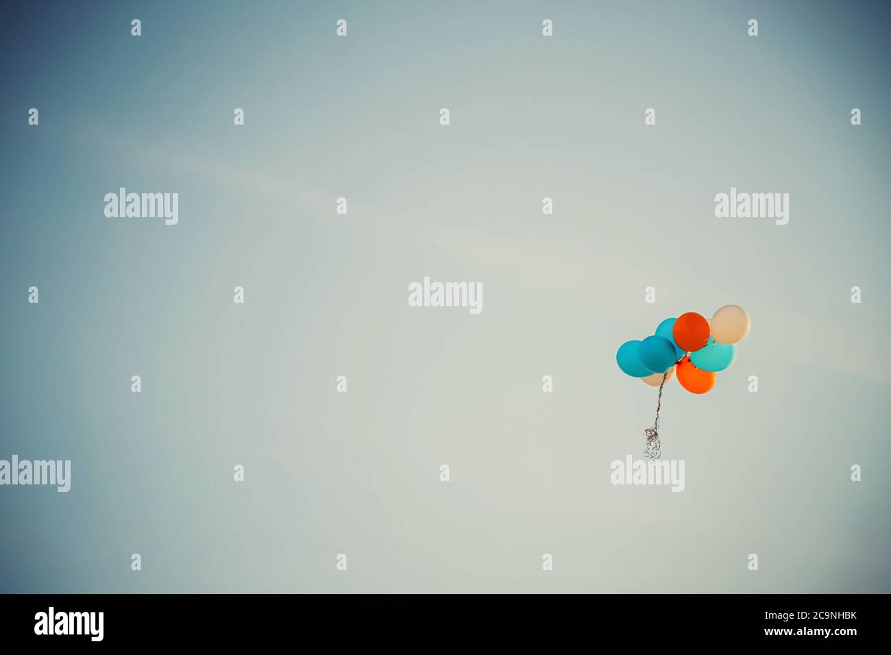 Lost bunch of painted balloons in a blue sky flying away with empty space for text Stock Photo