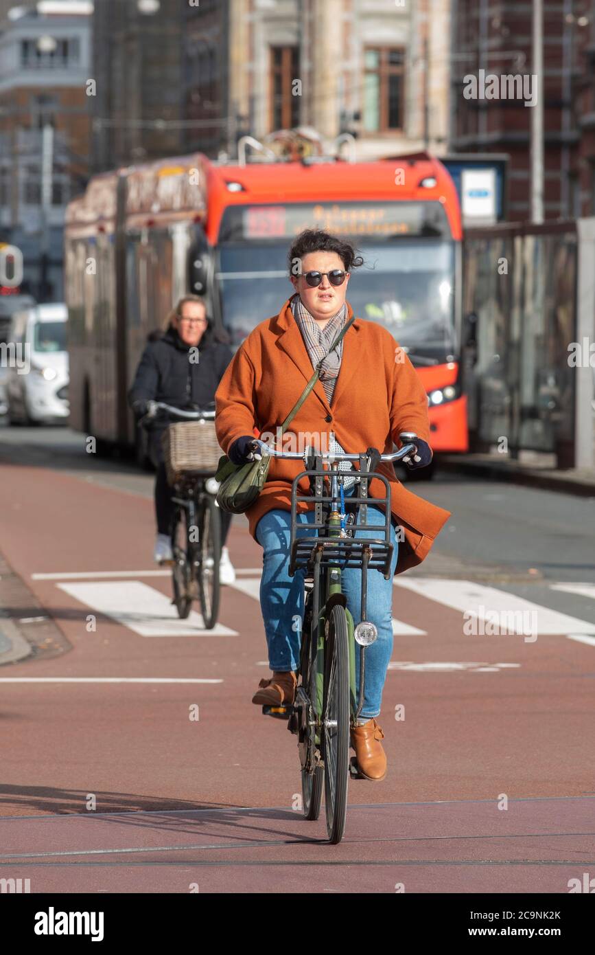 A woman in an orange coat rides her bicycle in Amsterdam, Netherlands. The color orange is the traditional color of the Dutch royal family, and hence Stock Photo