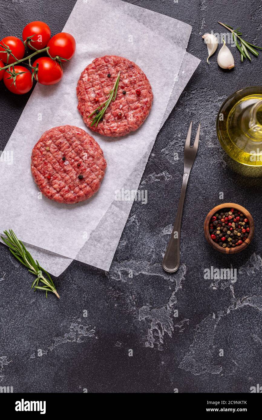 Fresh raw meat burger cutlet with herbs and spices on the black stone board, top view Stock Photo