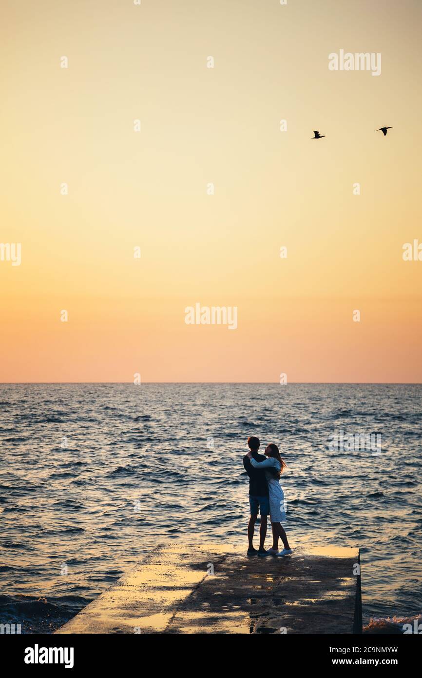 Silhouette of couple standing at the pier, watching the sunrise at the ...