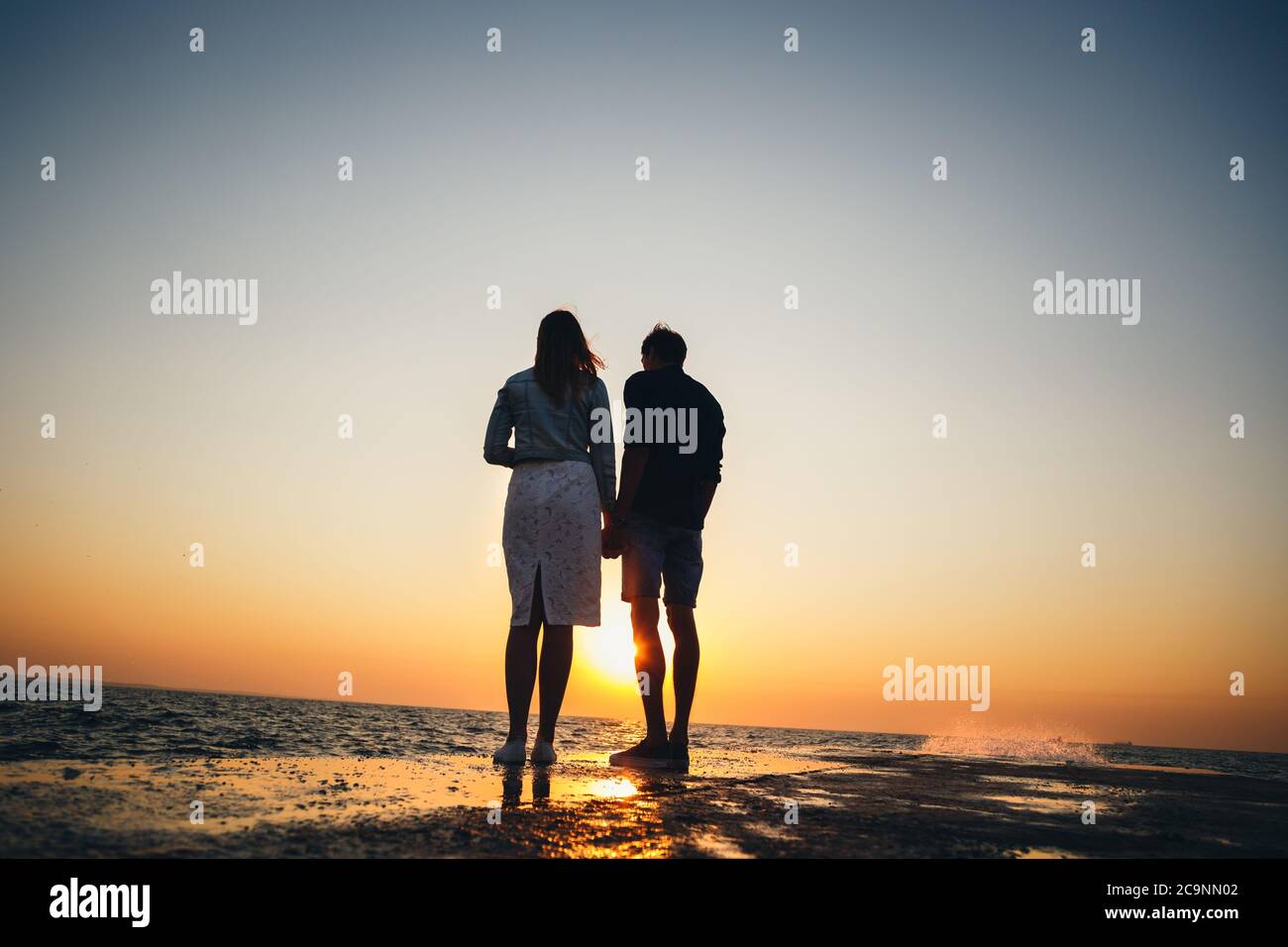Silhouette of couple standing at the pier, watching the sunrise at the ...