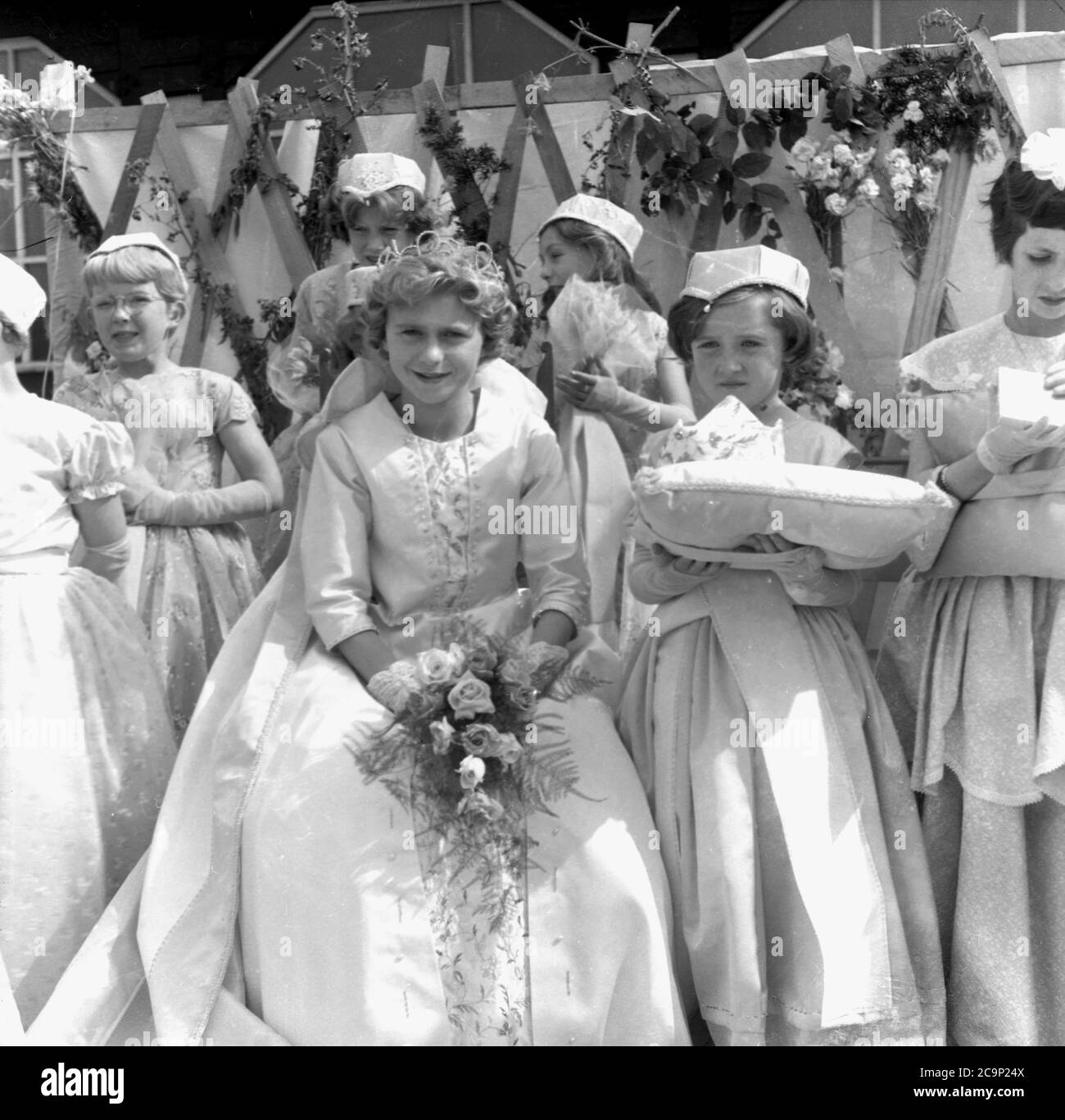 1950s, historical, on a platform outside a wooden sports pavillion at Farnworth, Lancashire, young girls dressed in gowns gather together for the Rose Queen ceremony. The 'Rose Queen' would lead the traditional procession or parade known as a 'Walking Day', celebrations which were common in the North West of England, UK in this era. An annual event, some date back to the 1830s where they were church parades connected to the childrens Sunday Schools and many are still held today. Stock Photo
