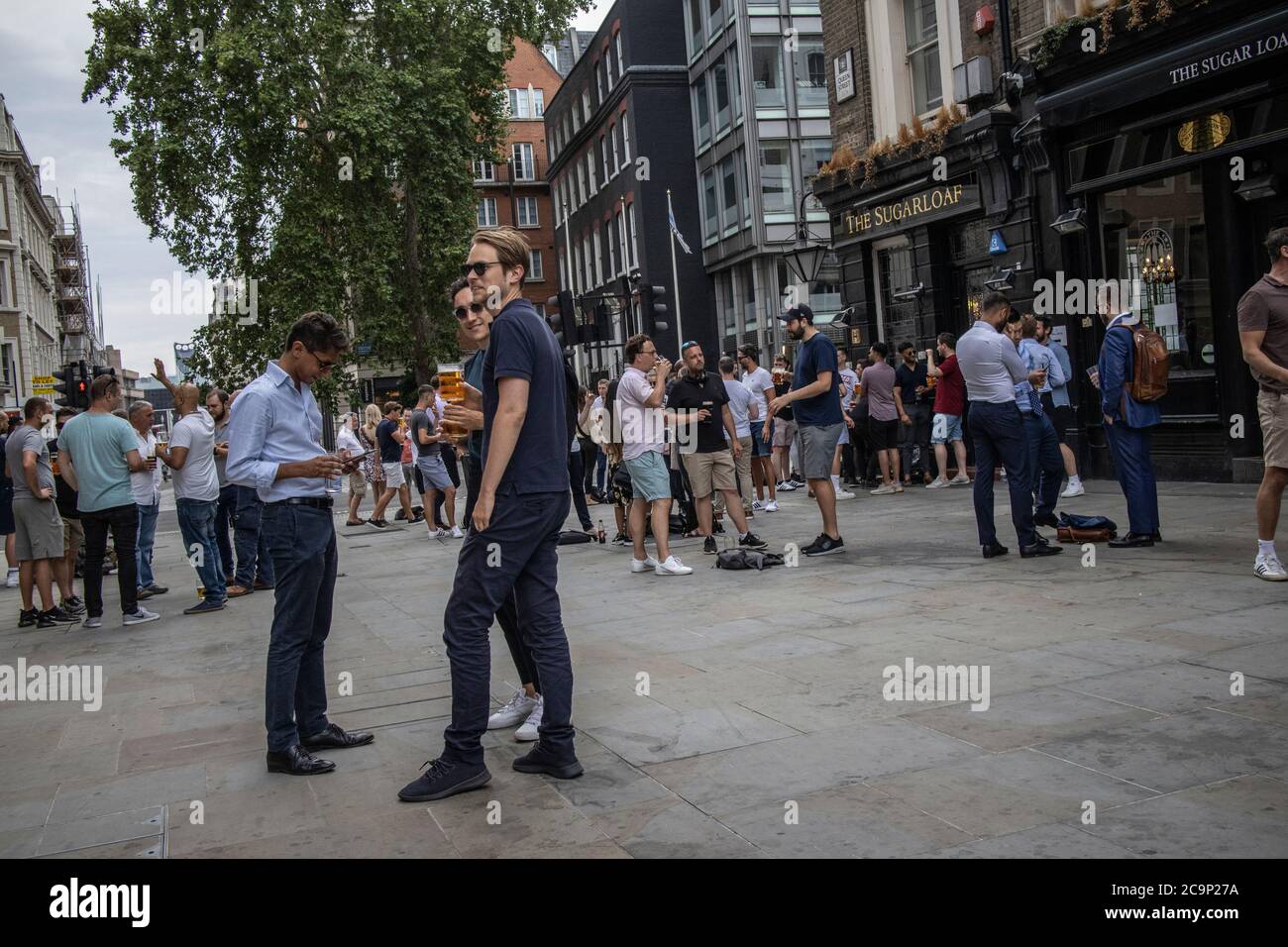 City workers enjoy drinking at the Sugarloaf pub whilst outside socially distanced on a summers Friday evening on Queen Street, London, EC4 Stock Photo