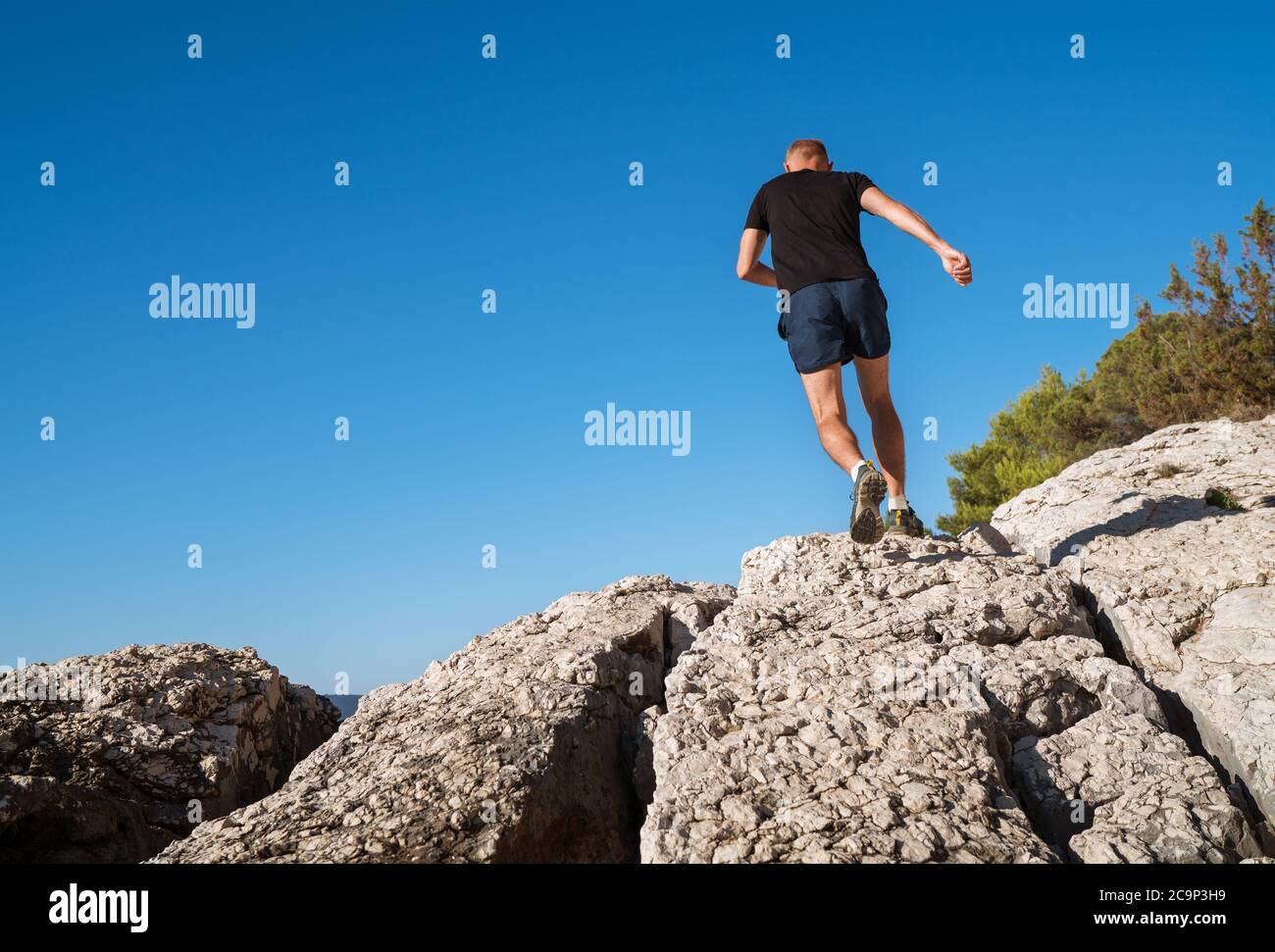 Active mountain skyrunner dressed black t-shirt and running shoes jogging the cliff summit during the morning scamper. Sporty people activities a wide Stock Photo
