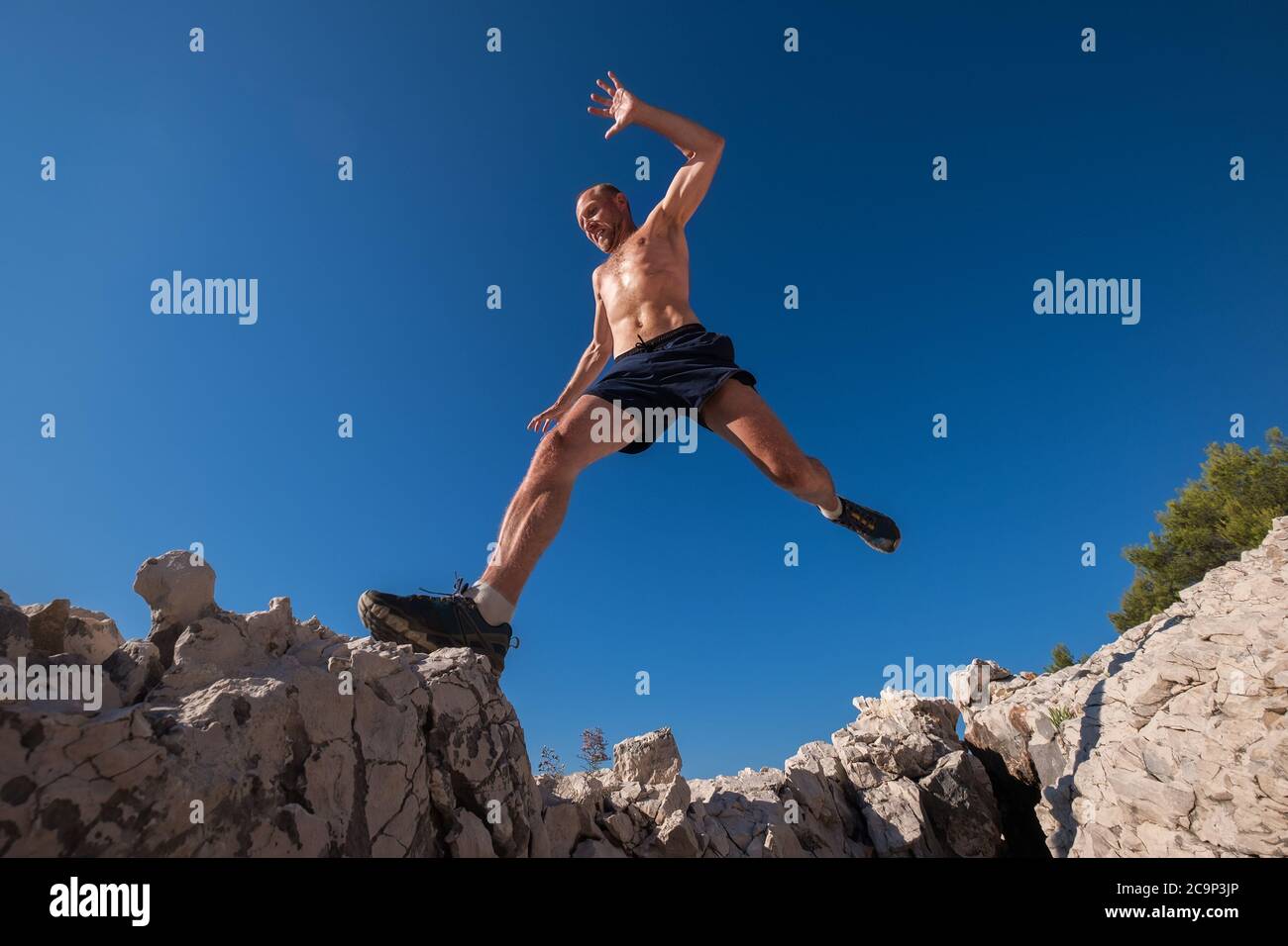 Active fast running mountain sweaty body muscular runner jumping over the cleft cliff during the morning jogging. Sporty people activities wide angle Stock Photo