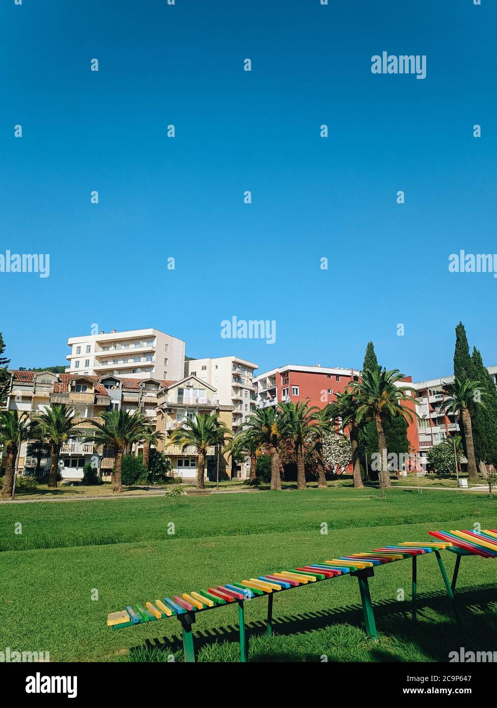 Yugoslavian houses in the center of Budva in Montenegro, next to the city park and green date palms, with a green lawn and blue skies in summer. Stock Photo
