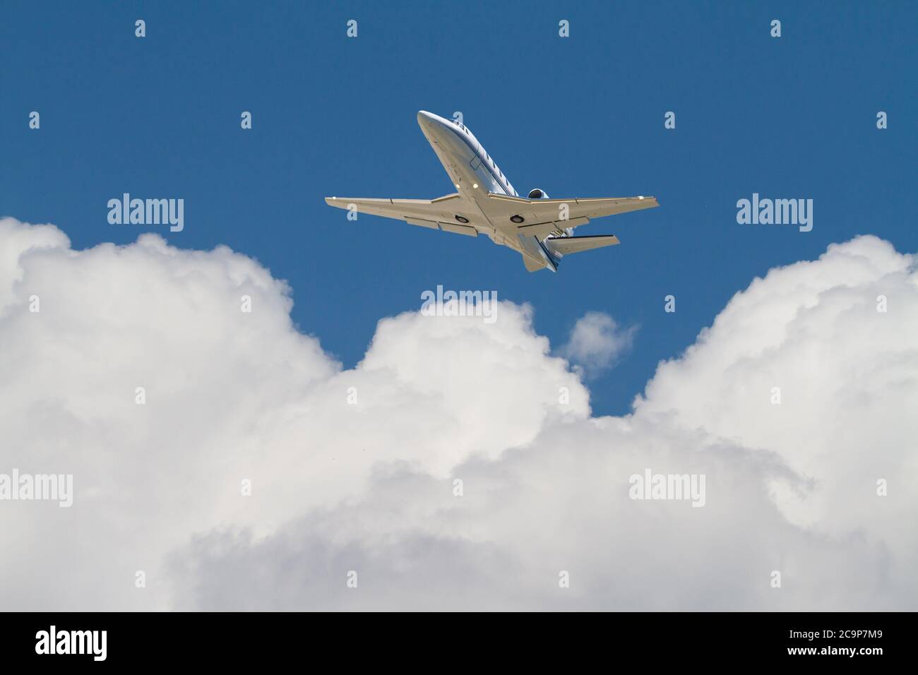 A corporate jet flies above puffy, white clouds in a deep blue sky. Stock Photo