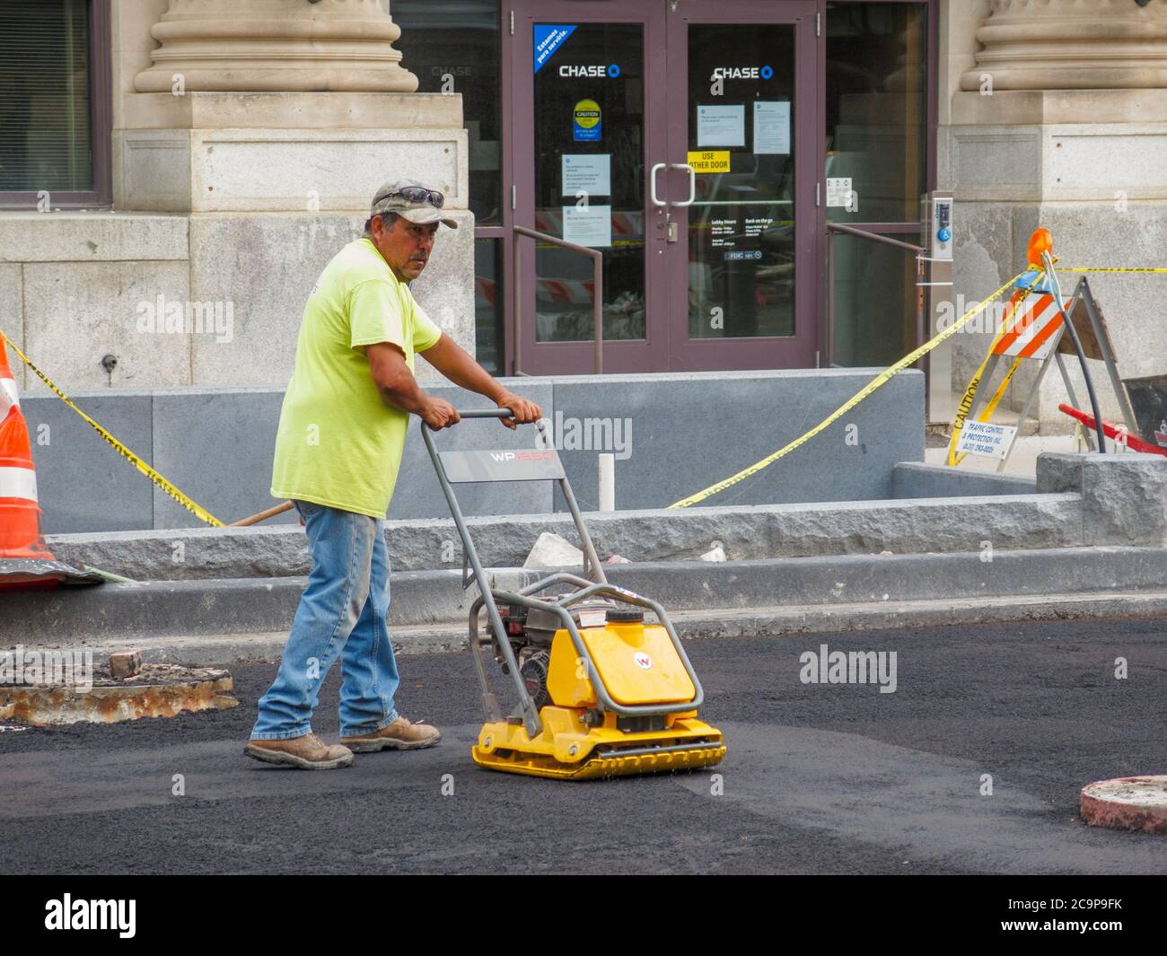 Construction worker using power tamper to tamp freshly laid asphalt