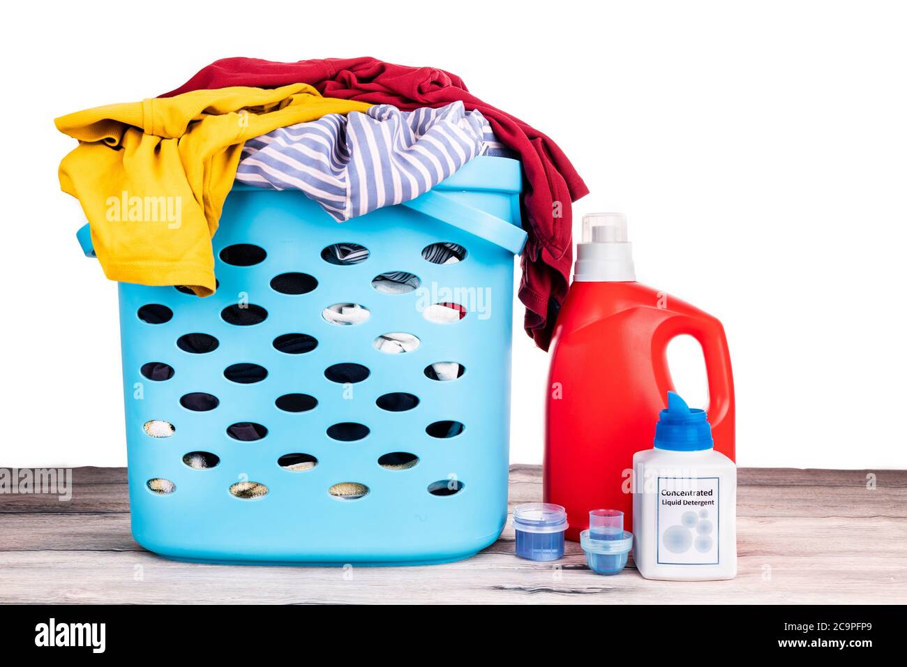 Compact concentrated laundry liquid detergent and regular liquid detergent next to basket full of apparels against white backgound Stock Photo