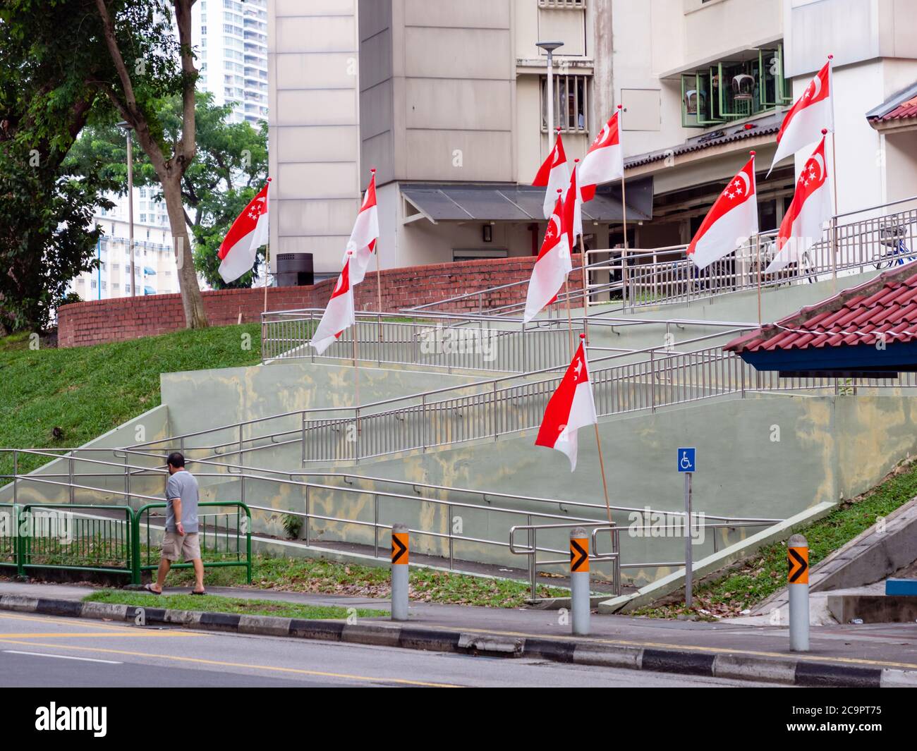 SINGAPORE – JUL 31, 2020 – A man walks past a row of Singaporean national flags placed at Sin Ming HDB residential estate in preparation for National Stock Photo