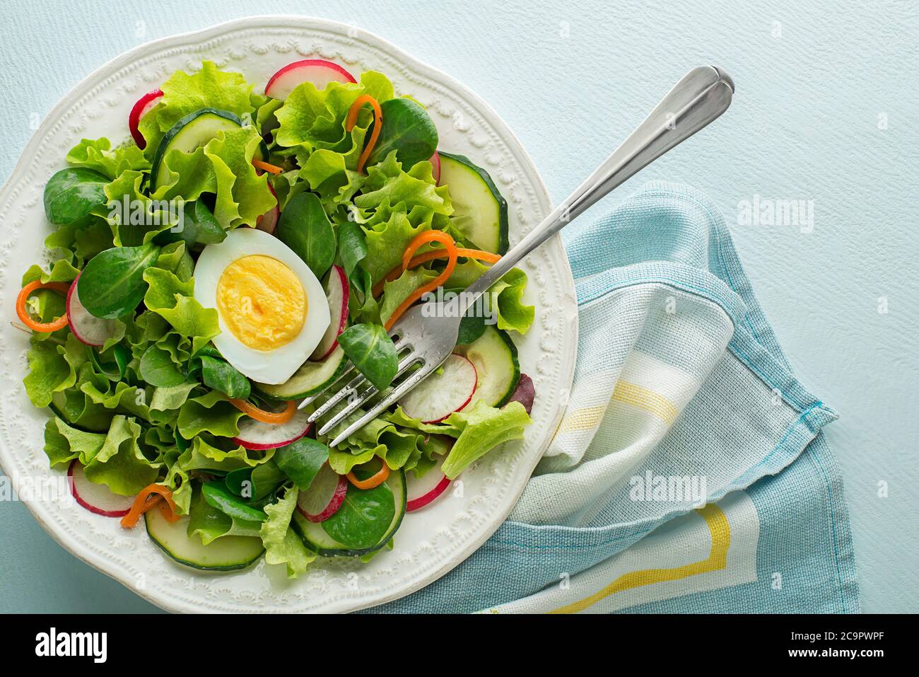 Healthy Green salad with fresh vegetables and boiled egg on blue table background Stock Photo