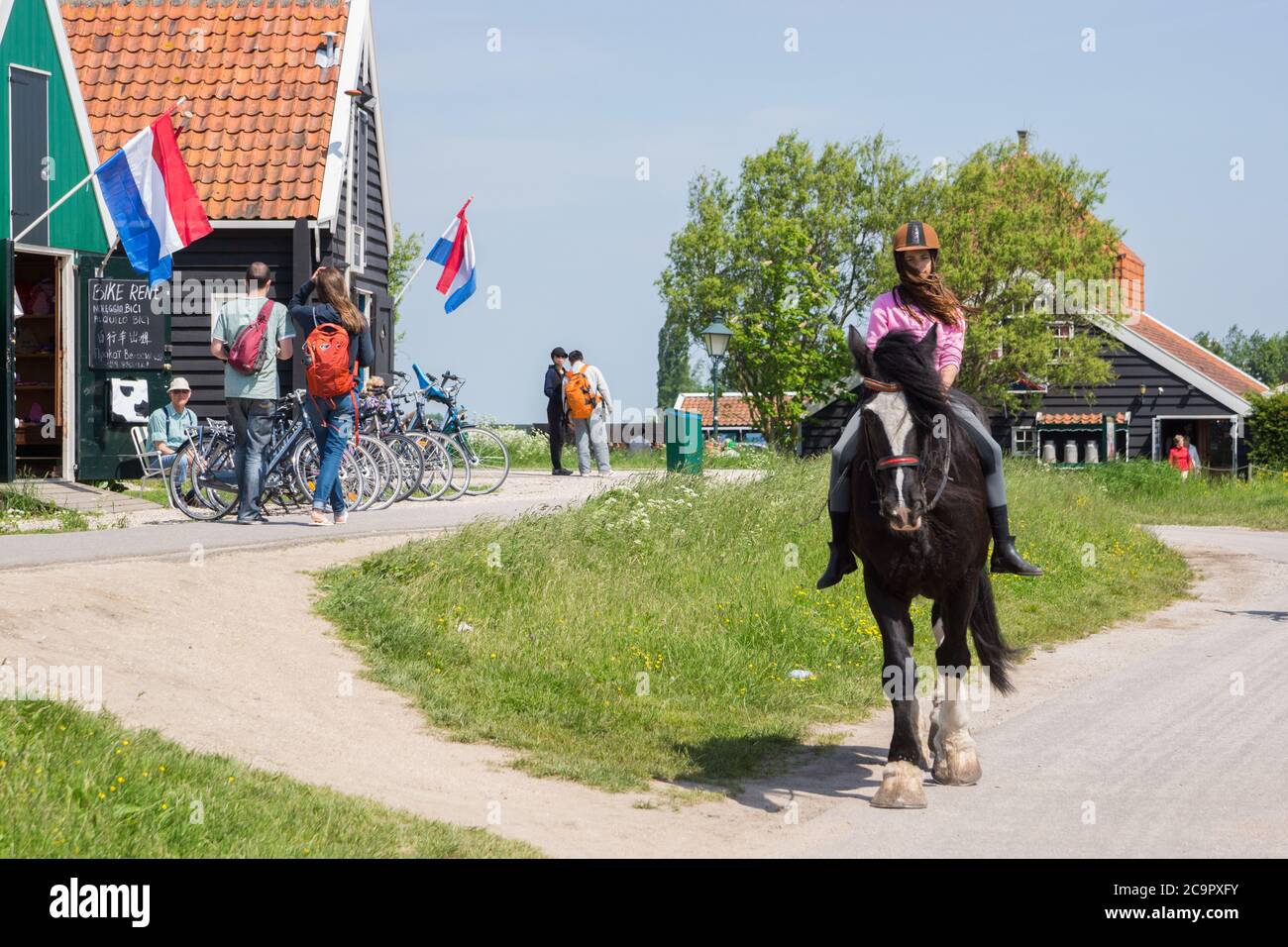 Young girl riding a horse at tourist village with houses and shops at Zaanse Schans, Zaandam, the Netherlands Stock Photo