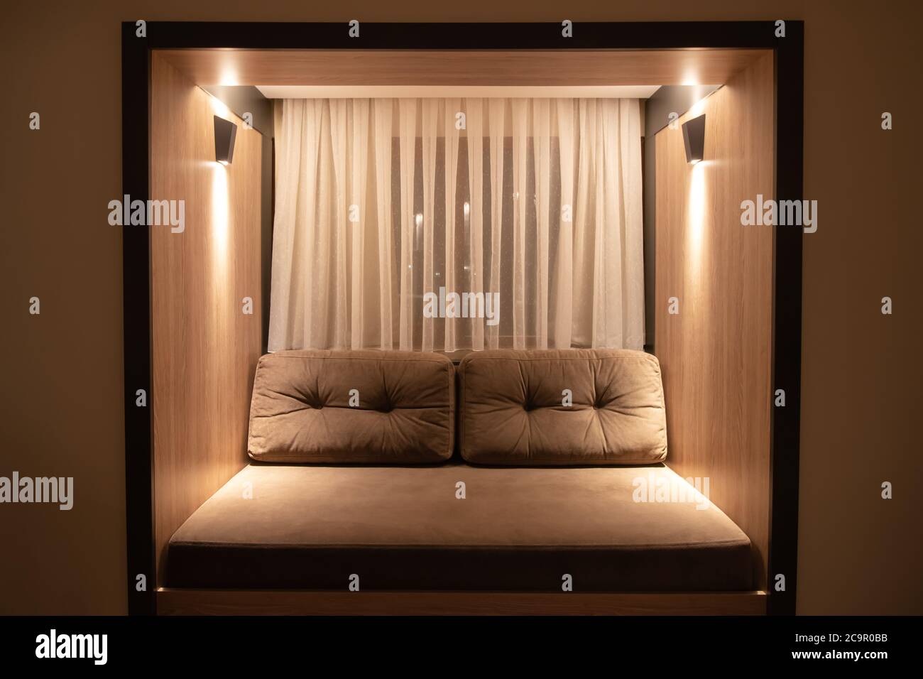 Living room interior with sofa and illumination, brown couch with pillows and soft lighting. Evening, twilight. A window with curtains Stock Photo