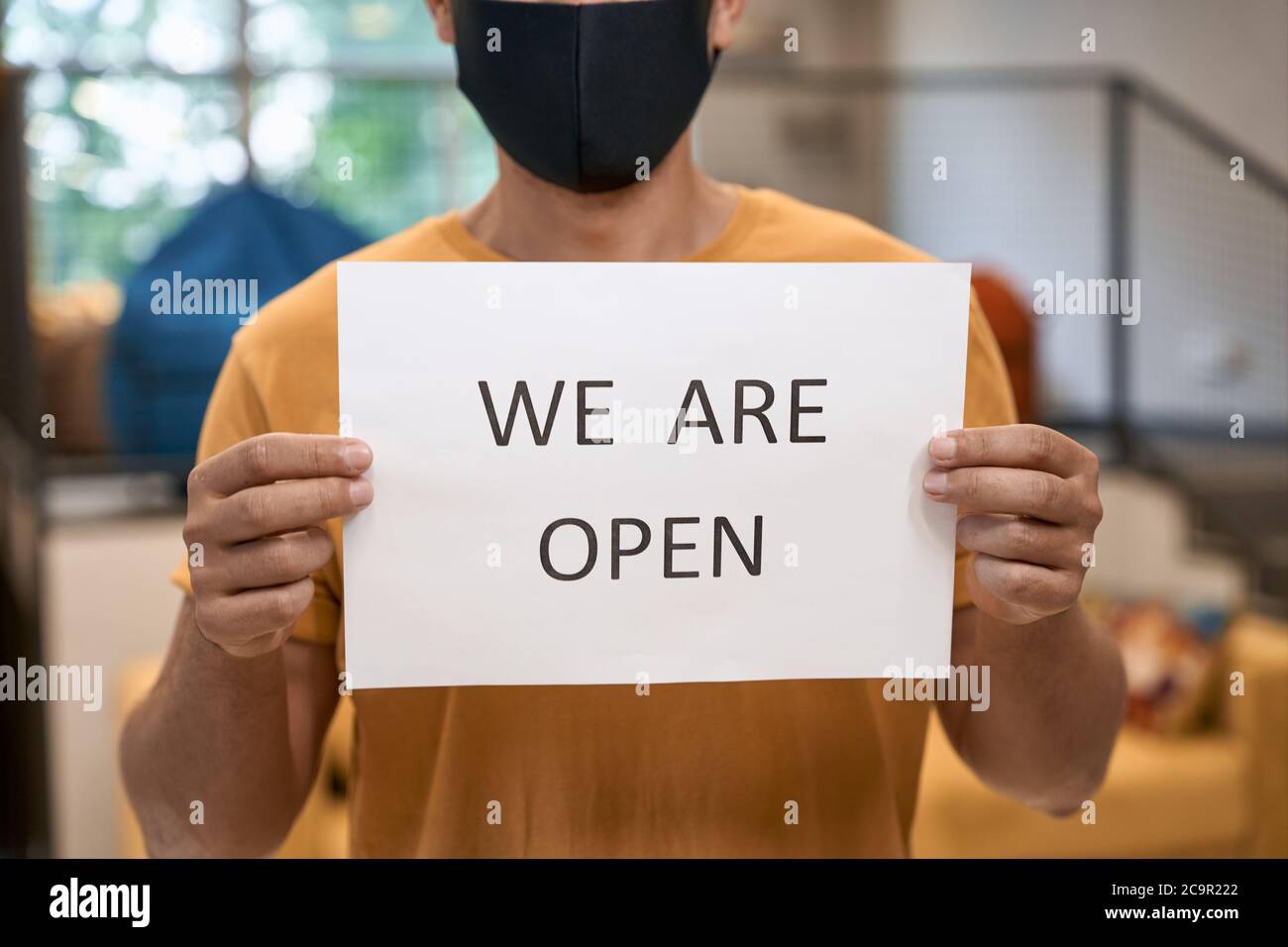 Business after lockdown. Close up shot of a male office worker in black protective mask showing paper with text WE ARE OPEN at camera, standing in the Stock Photo
