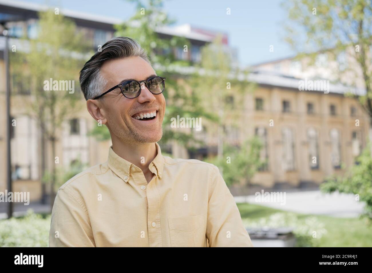 Portrait of handsome mature man wearing stylish eyeglasses, walking on the street, laughing. Positive lifestyle concept Stock Photo