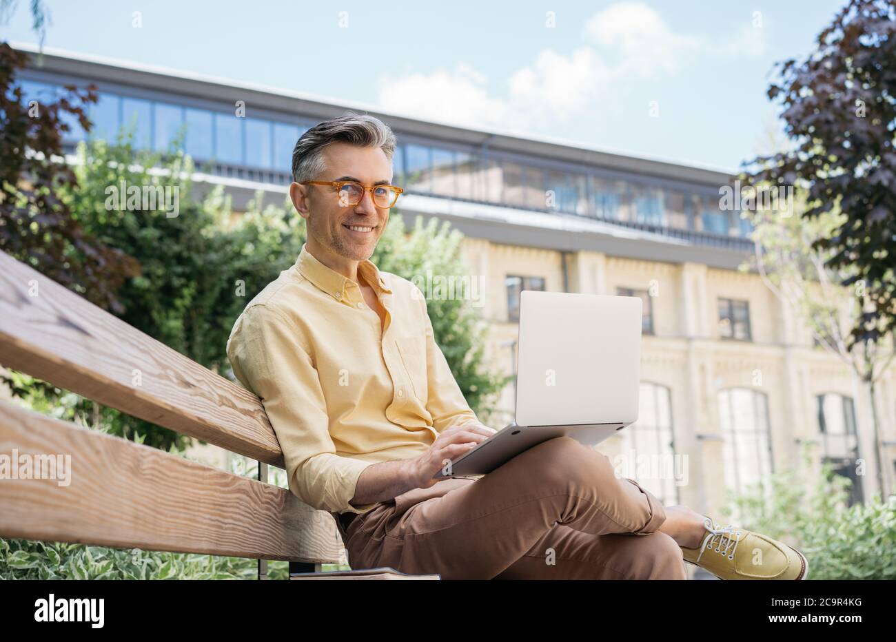 Confident freelancer copywriter using laptop computer, typing on keyboard, looking at camera, smiling Stock Photo