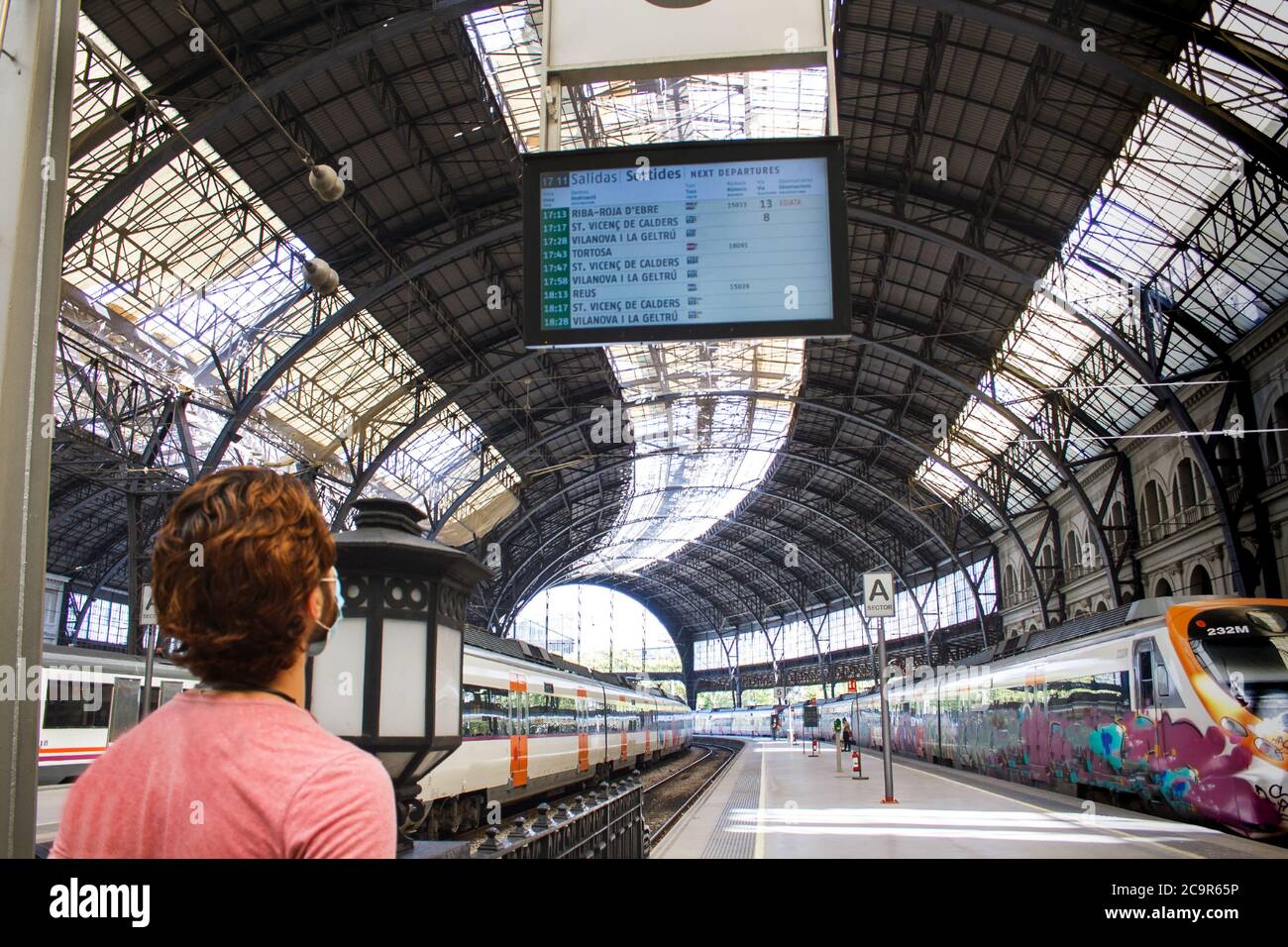 Young man checking train station timetables. Panoramic view. Travel safe covid times. Stock Photo