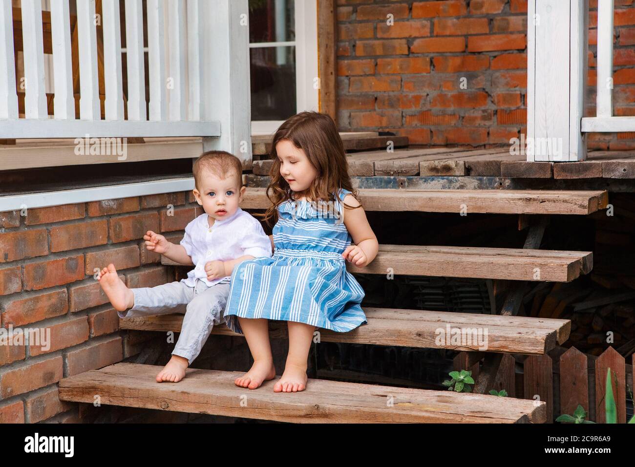 Cute little brother and sister sitting on wooden staircase near porch ...