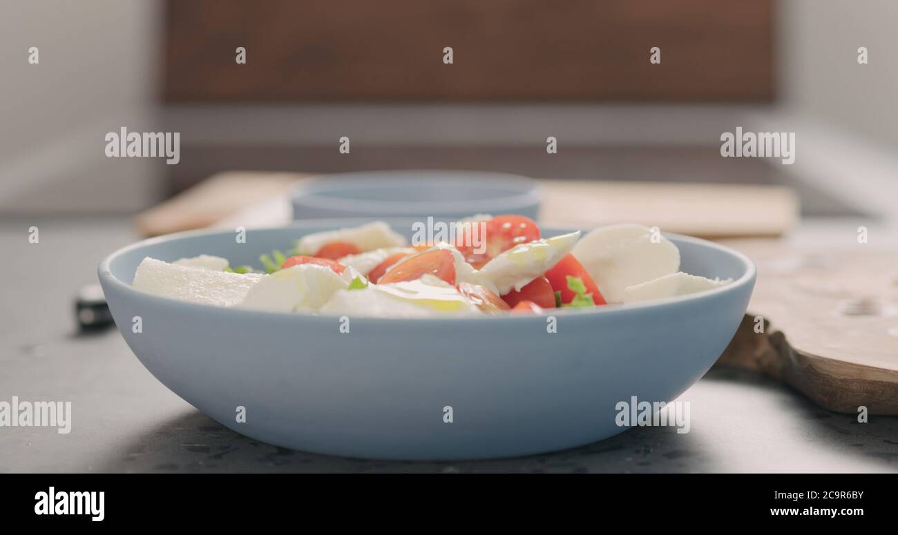 making salad with frisee lettuce, tomatoes amd mozzarella in a blue bowl on kitchen countertop Stock Photo