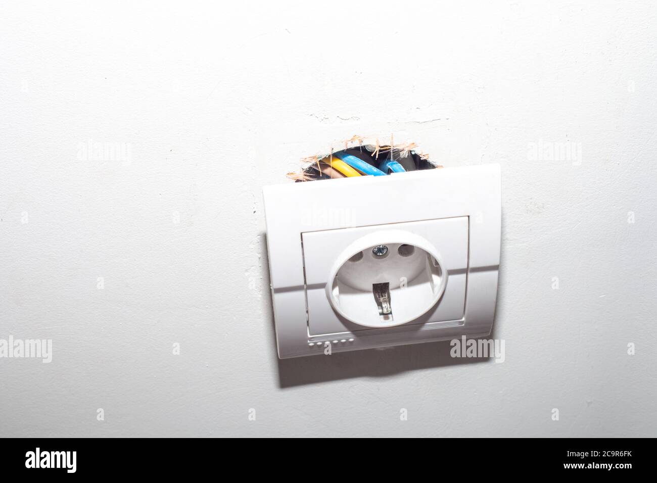 Broken electric socket torn from white wall. Fixing loose electrical