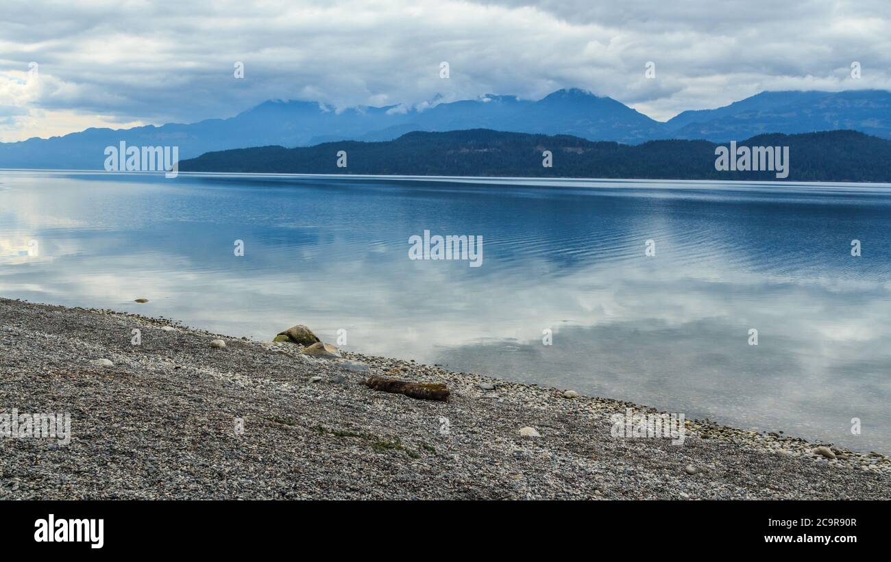 Camping side lake in Vancouver surrounded by mountains during summer day as the clouds are reflecting in the water Stock Photo