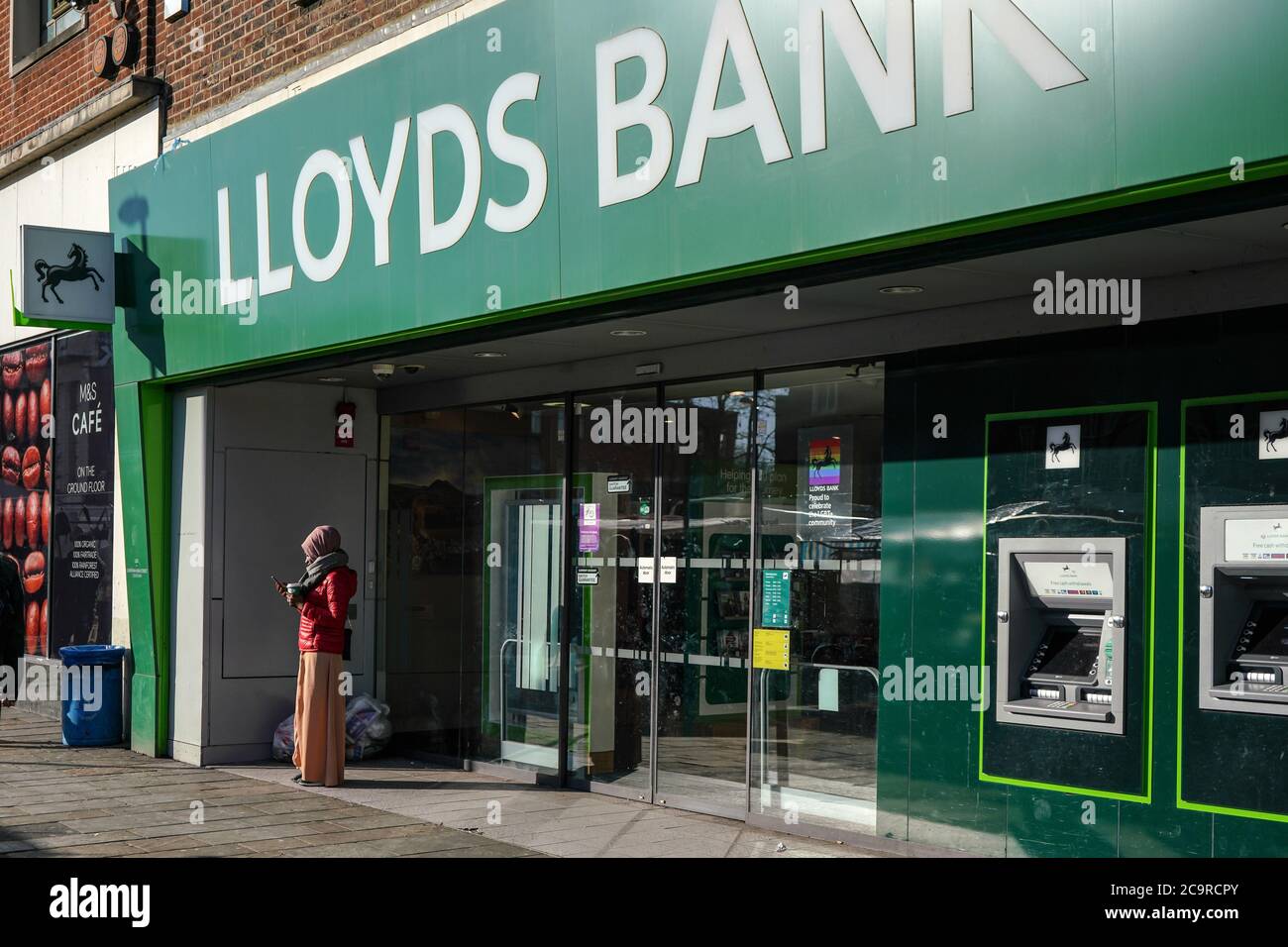 London, United Kingdom - February 03, 2019: Unknown woman checking her mobile in front of Lloyds Bank branch at Lewisham on sunny morning. It is one o Stock Photo