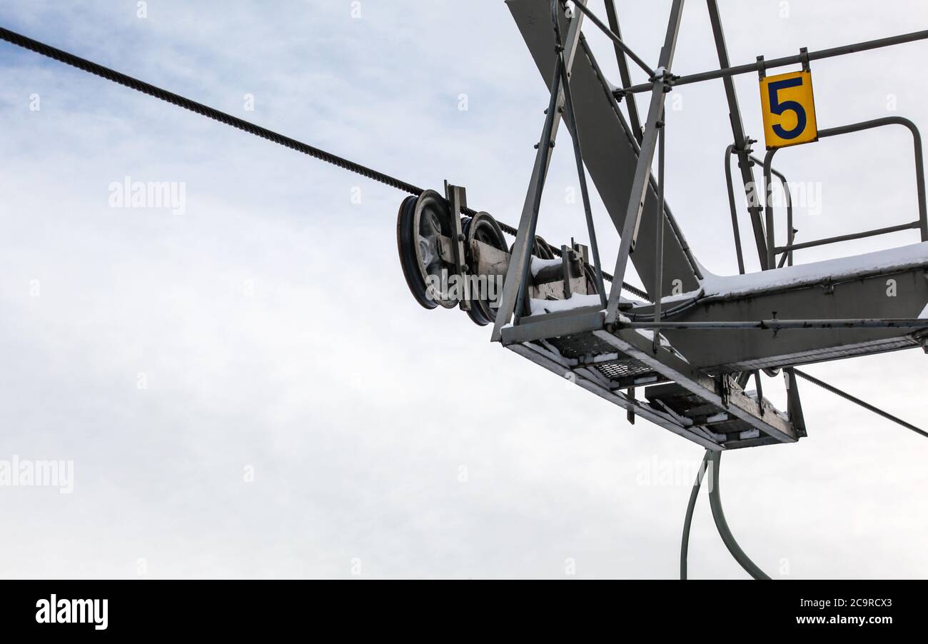 Steel ropes over wheels in mechanism on top of ski lift support pillar, number 5 on yellow plate. Wide banner with space for text left down Stock Photo