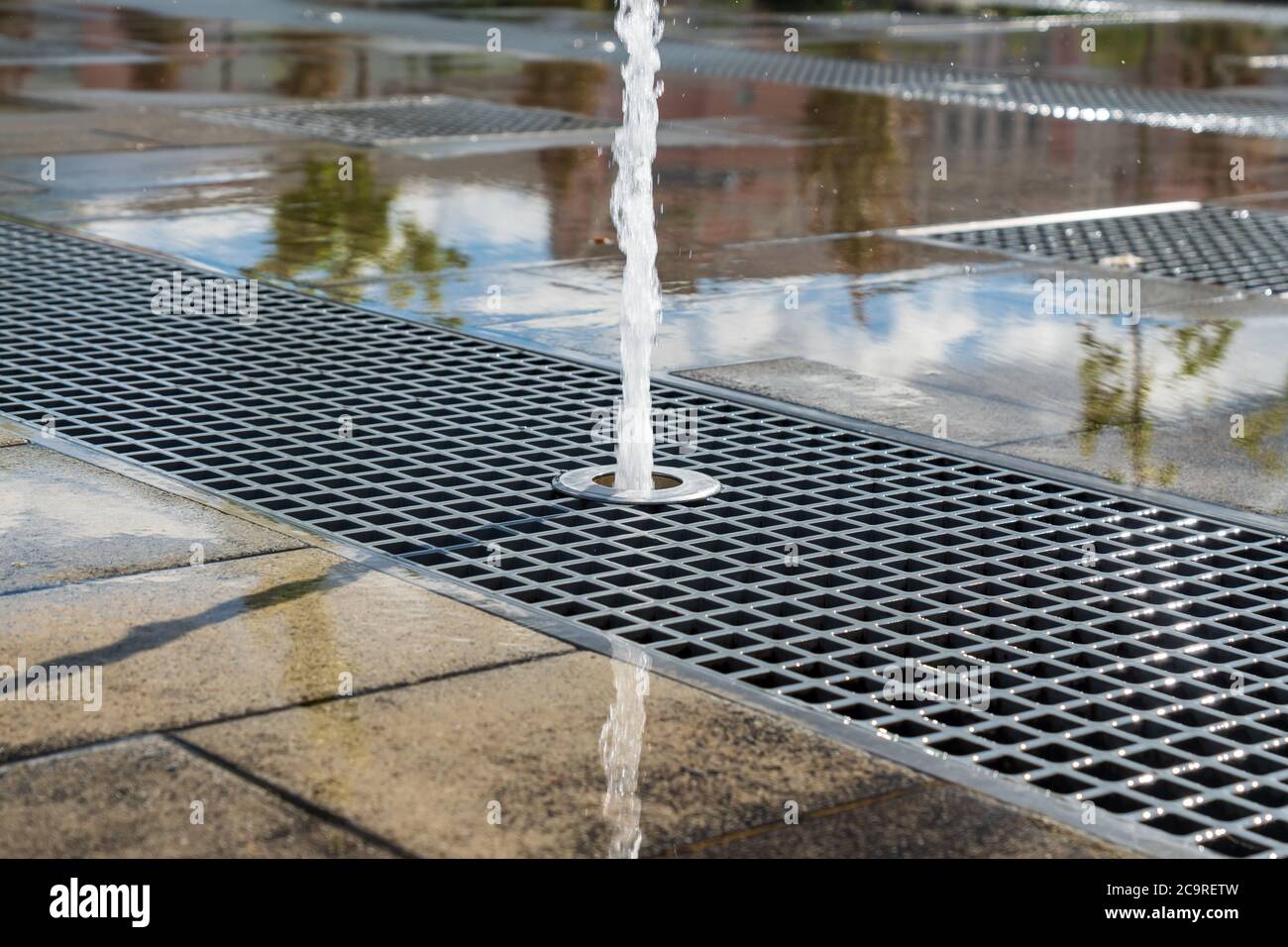 Vertical water streams of dry fountain, close up view. Streams flowing out of stainless grate. Stock Photo
