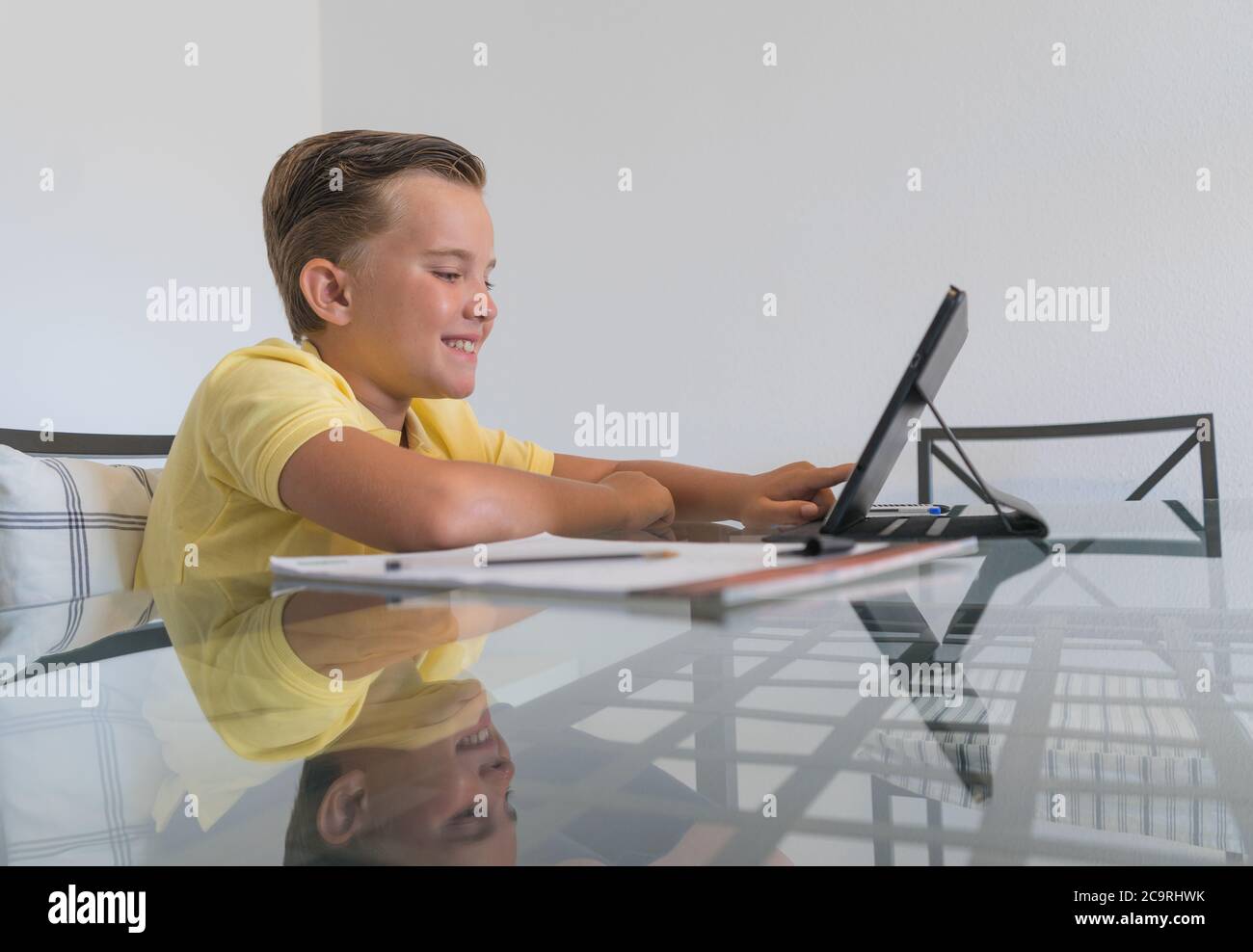 Boy talking with classmate during video call on tablet and discussing homework while sitting at table in modern light room. Stock Photo