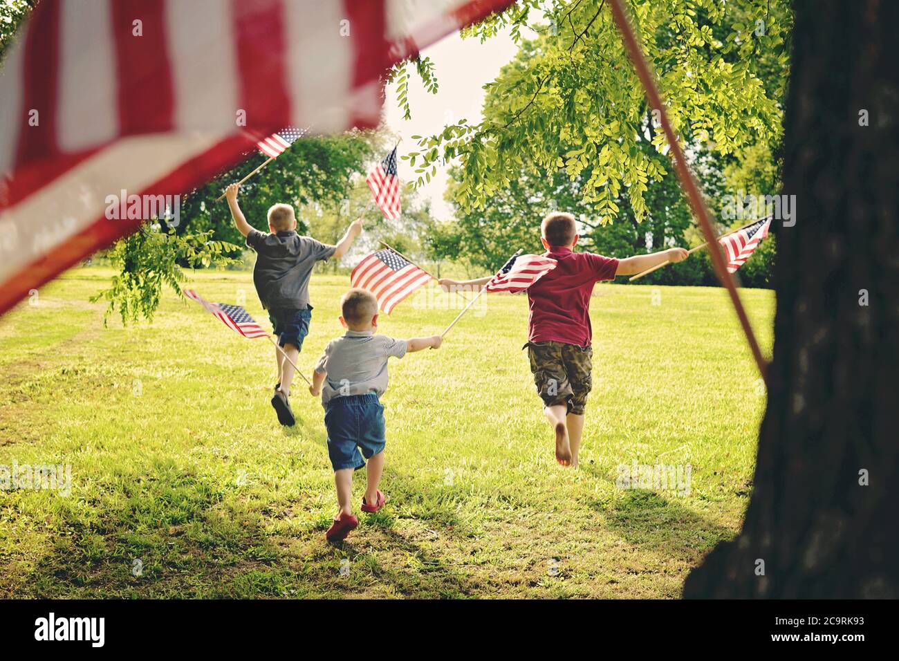 Three boys holding American Flags enthusiastically while waving them Stock Photo