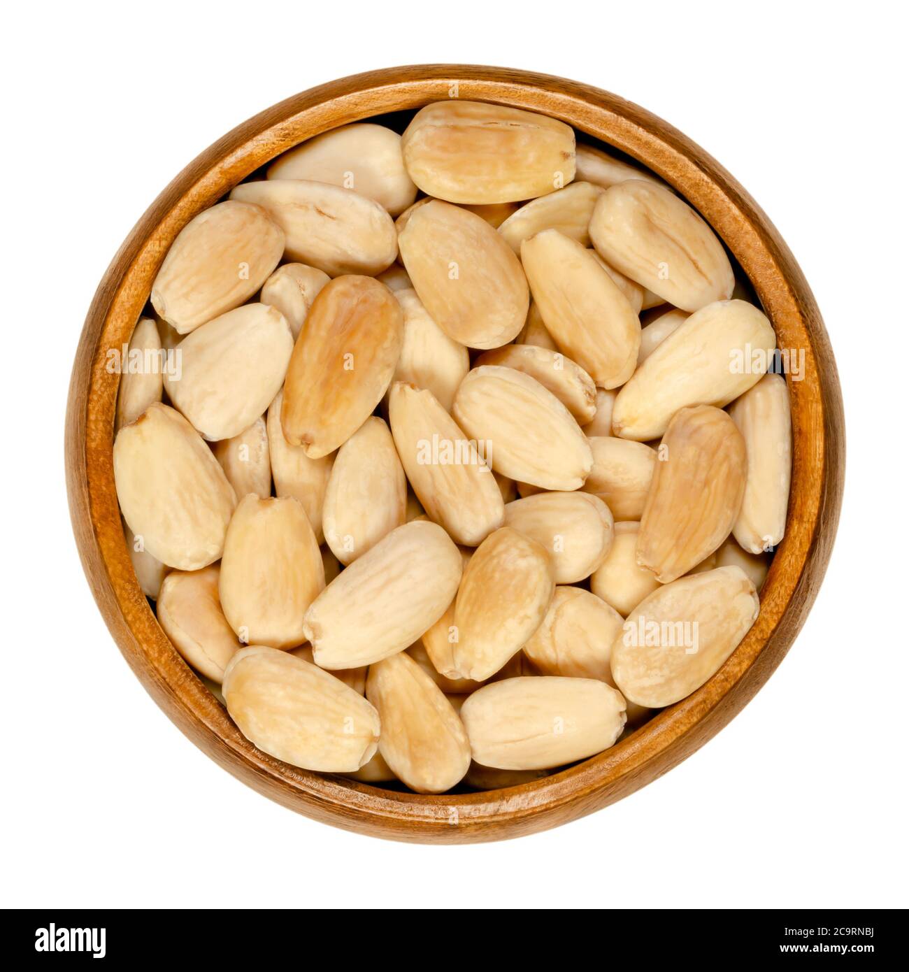 Blanched and roasted almonds in a wooden bowl. Whole seeds, skinned and roasted, ready to eat as snack or dessert. Prunus dulcis. Close-up, from above Stock Photo