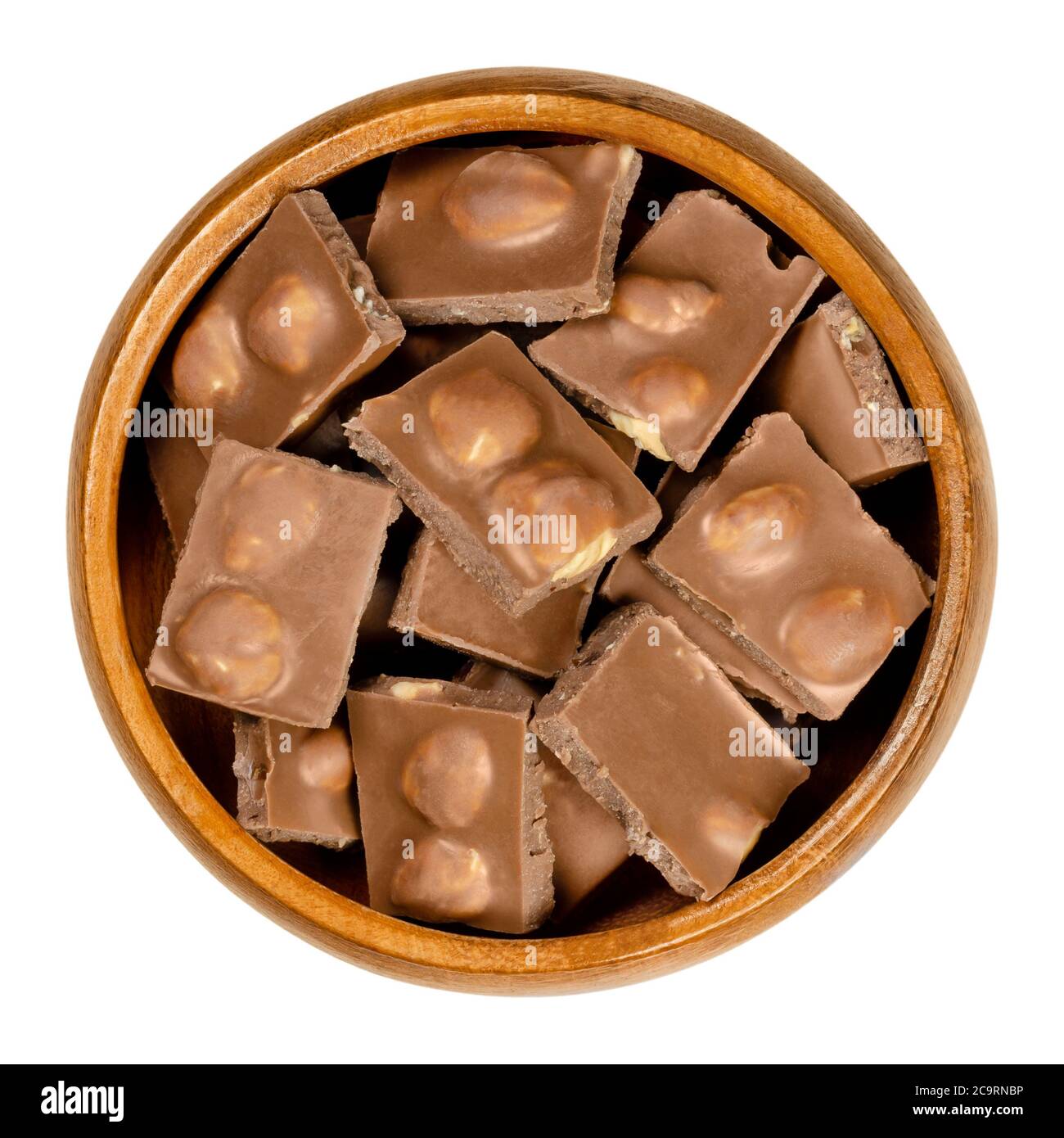 Hazelnut milk chocolate, bars broken into pieces, in wooden bowl. Small segments of candy bar. Milk chocolate with whole roasted hazelnuts. Stock Photo
