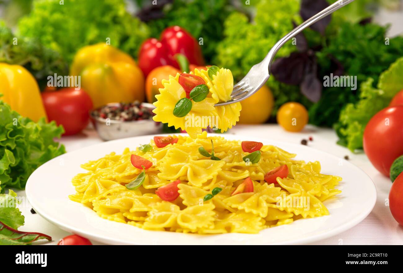 Plate of italian pasta, farfalle on fork with tomatoes and basil Stock Photo