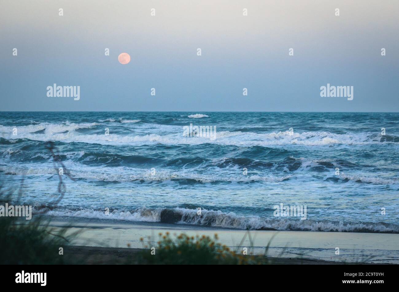 Rise of full moon over the sea at sandy beach and rough waves. Southern France. Stock Photo