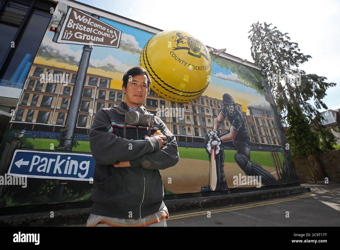 Graffiti artist Silent Hobo poses for a photo in front of his painted mural at Bristol County Ground. Stock Photo