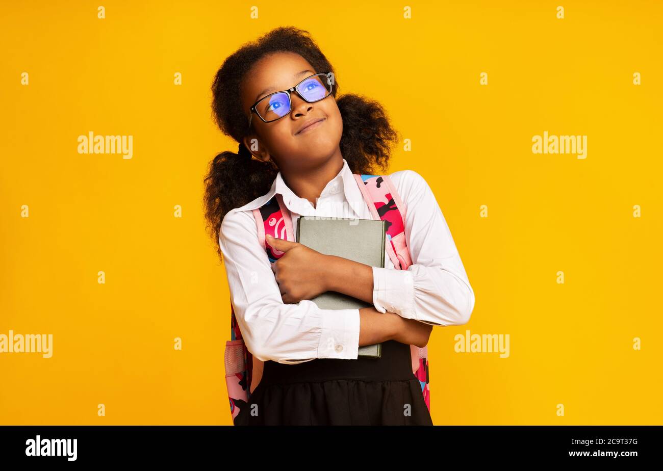 Happy African Schoolgirl Embracing Book Over Yellow Studio Background Stock Photo