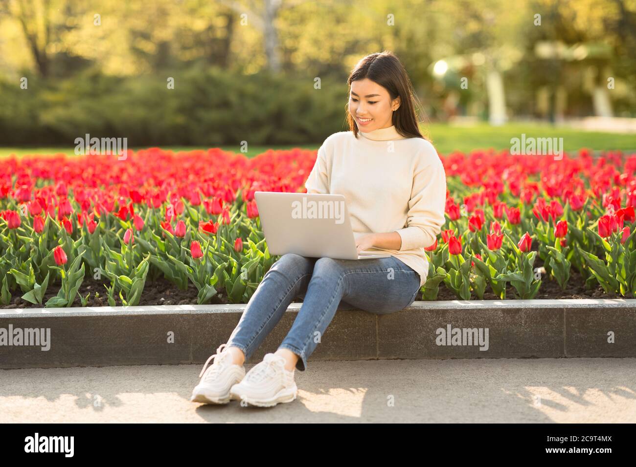 Asian girl using laptop, sitting on parapet in park Stock Photo - Alamy