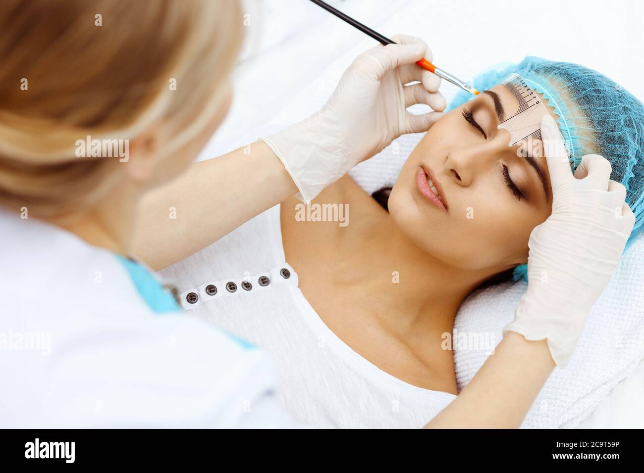 Professional beautician is going to correct eyebrow line at woman face ...