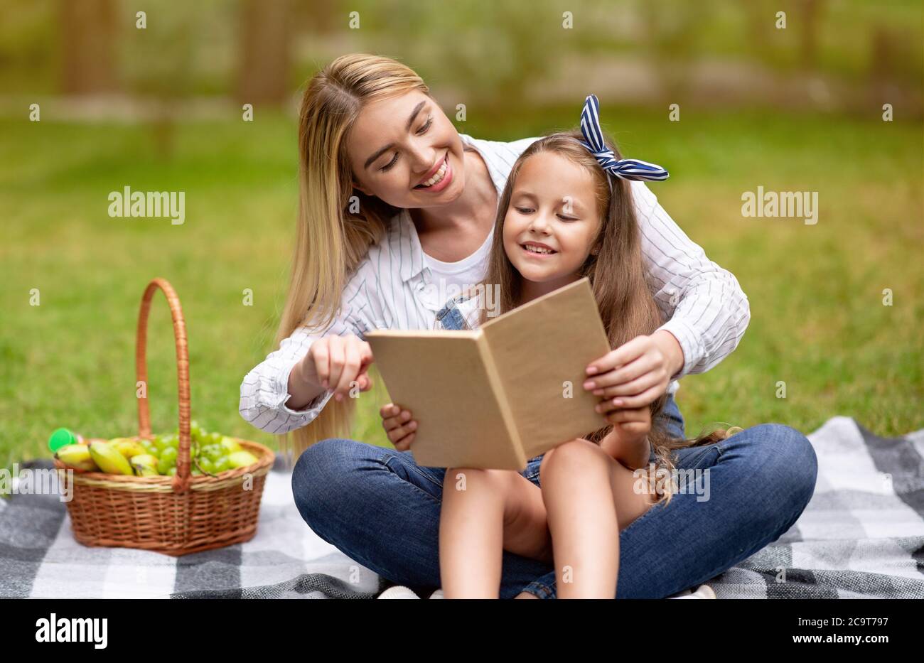 Mom And Daughter Reading Book In Park Spending Time Together