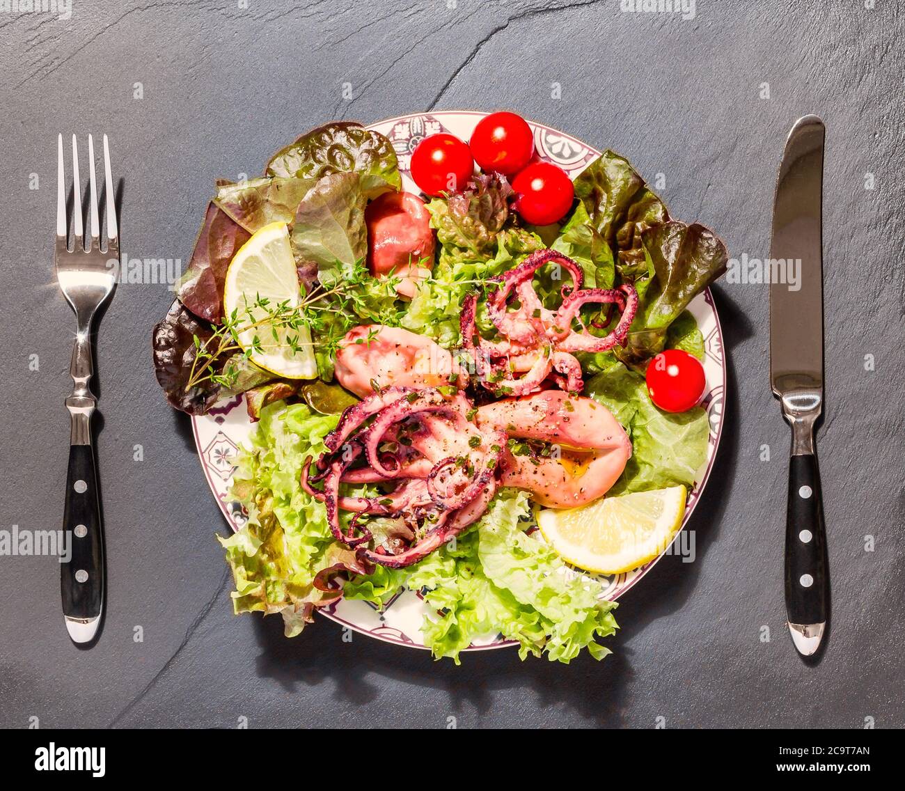 Octopus on blue plate with salad and lemon, on black slate Stock Photo
