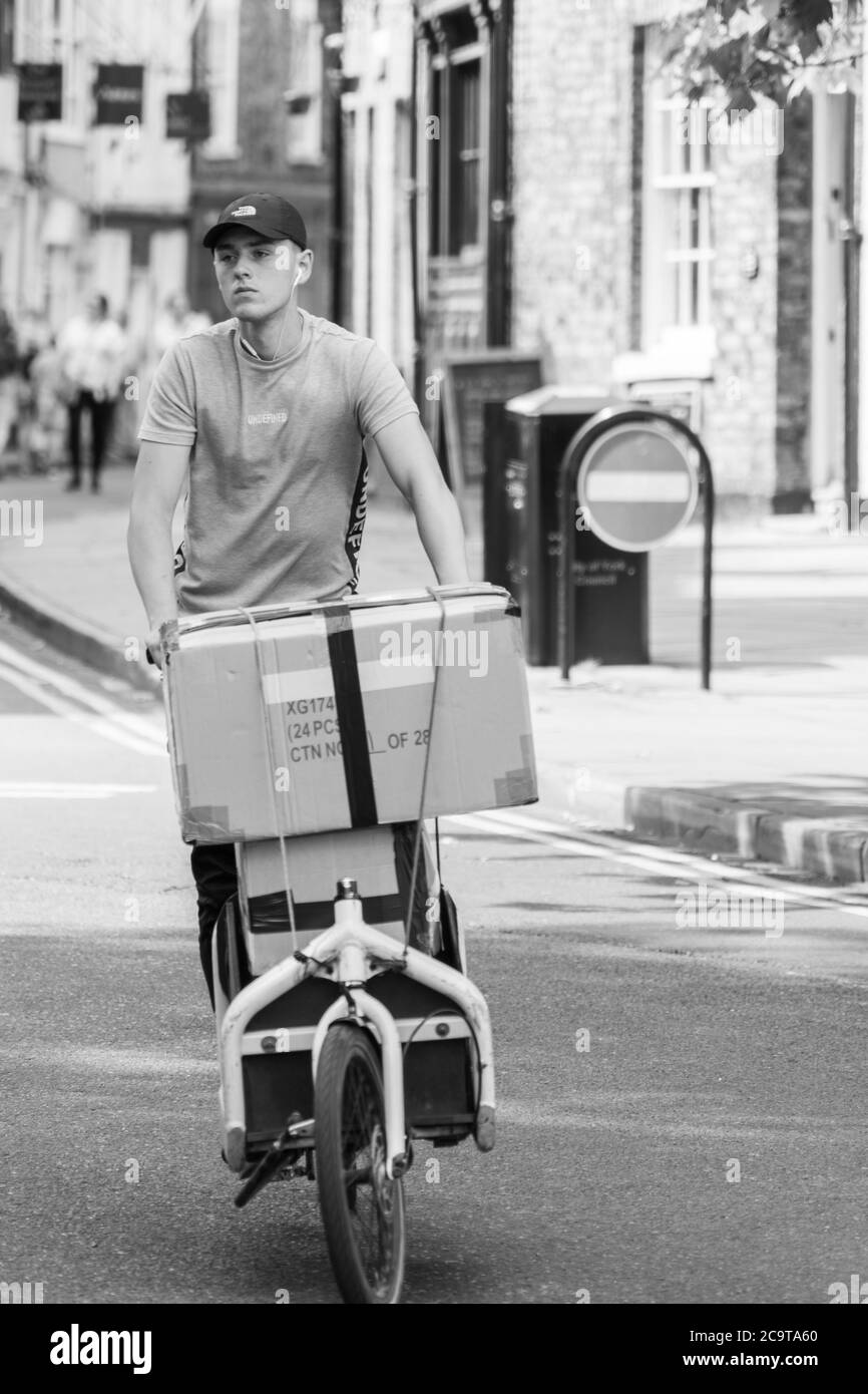 A young man delivering large parcels by bike along an inner-city Street, York, North Yorkshire, England, United Kingdom. Stock Photo