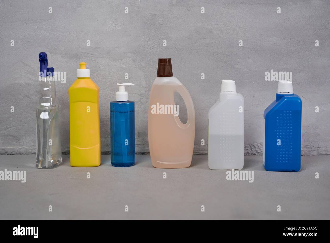 Cleaning supplies. Colorful plastic bottles with different detergents standing in a row on the floor against grey wall. Housework, house cleaning services and disinfection, housekeeping Stock Photo
