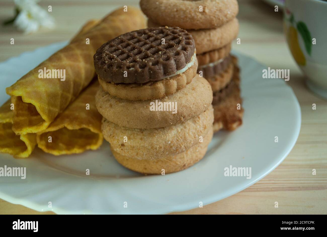 Waffle rolls and cookies on a white plate. Composition on a wooden background. Visible wood texture, waffle texture Stock Photo