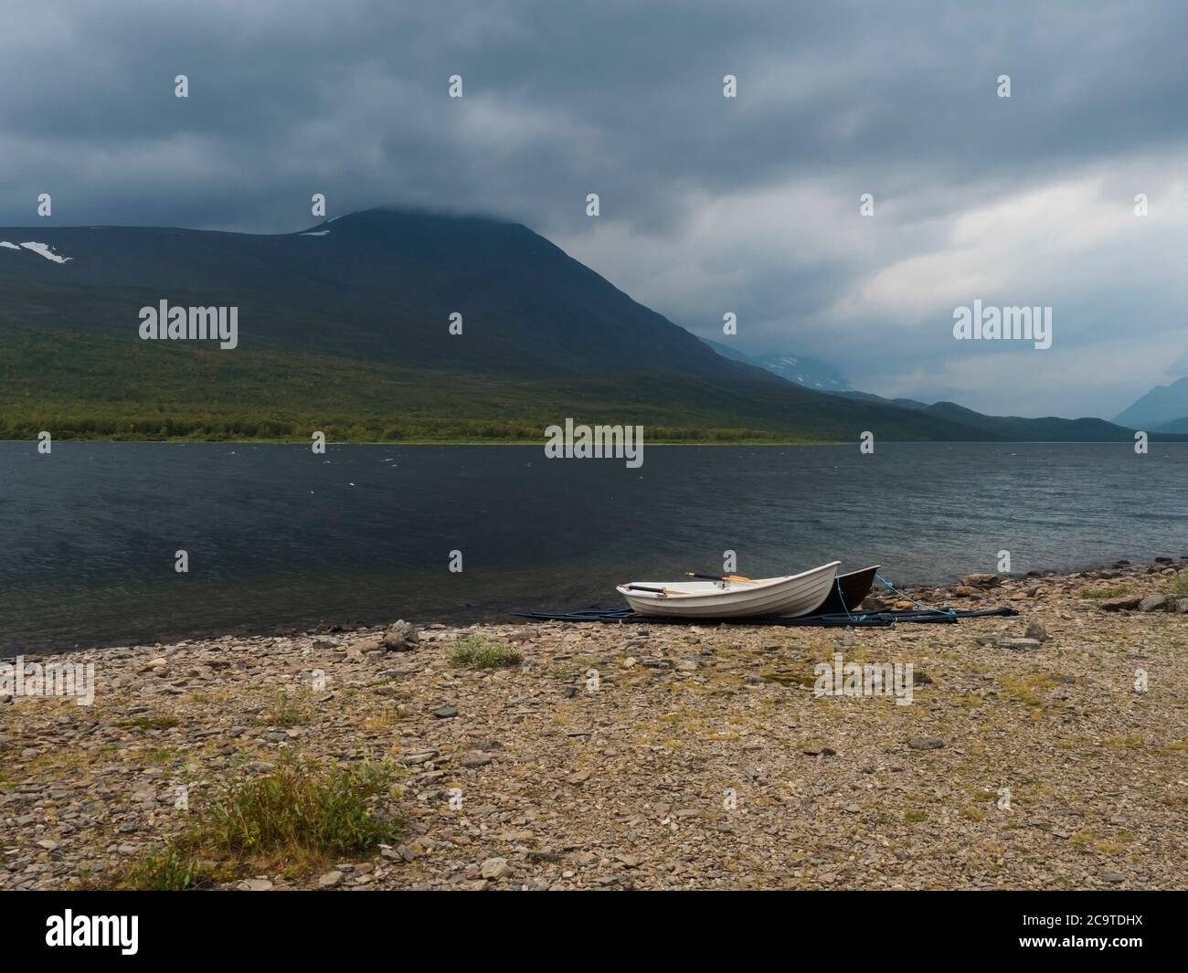 two rowing boats at Kungsleden hiking trail on bank of Teusajaure lake with birch tree forest and mountains. Lapland nature landscape in summer, moody Stock Photo