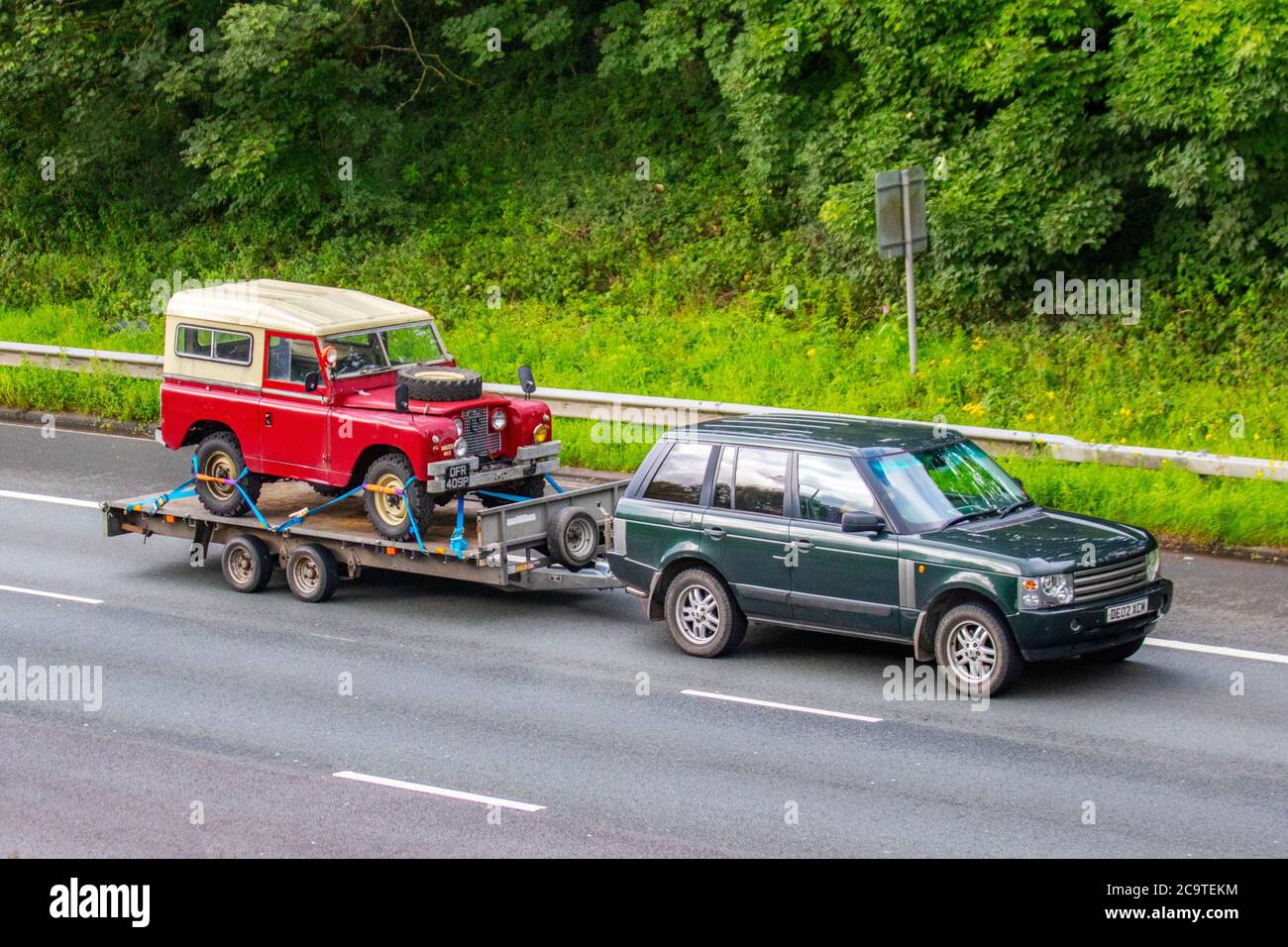 1996 90s red SWB Canvas Land Rover Series IIa pickup on a trailer towed by Land Rover Range Rover HSE TD6 Auto;  Vehicular traffic moving vehicles, cars driving a vehicle on UK roads, 90s classic motors, motoring on the M6 motorway highway network. Stock Photo