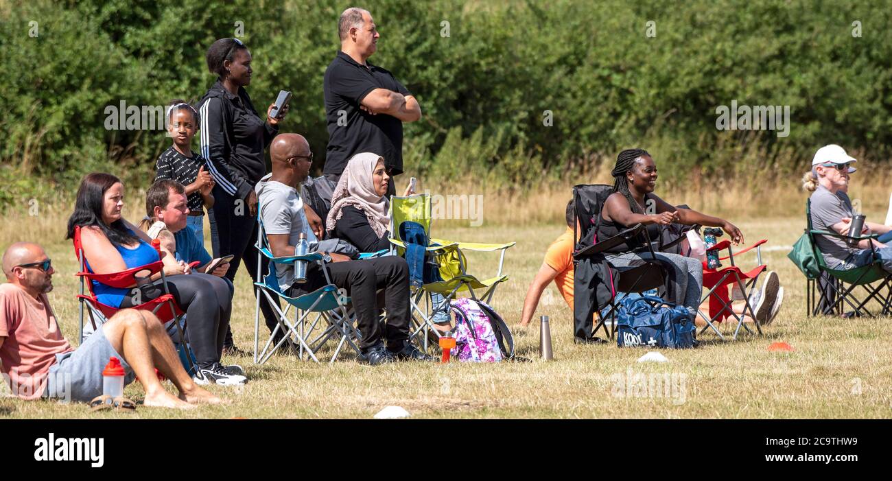 Basingstoke, Hampshire, England, UK. August 2020. People standing and sitting watch a children's soccer match as rules regarding lockdown of Coronavir Stock Photo