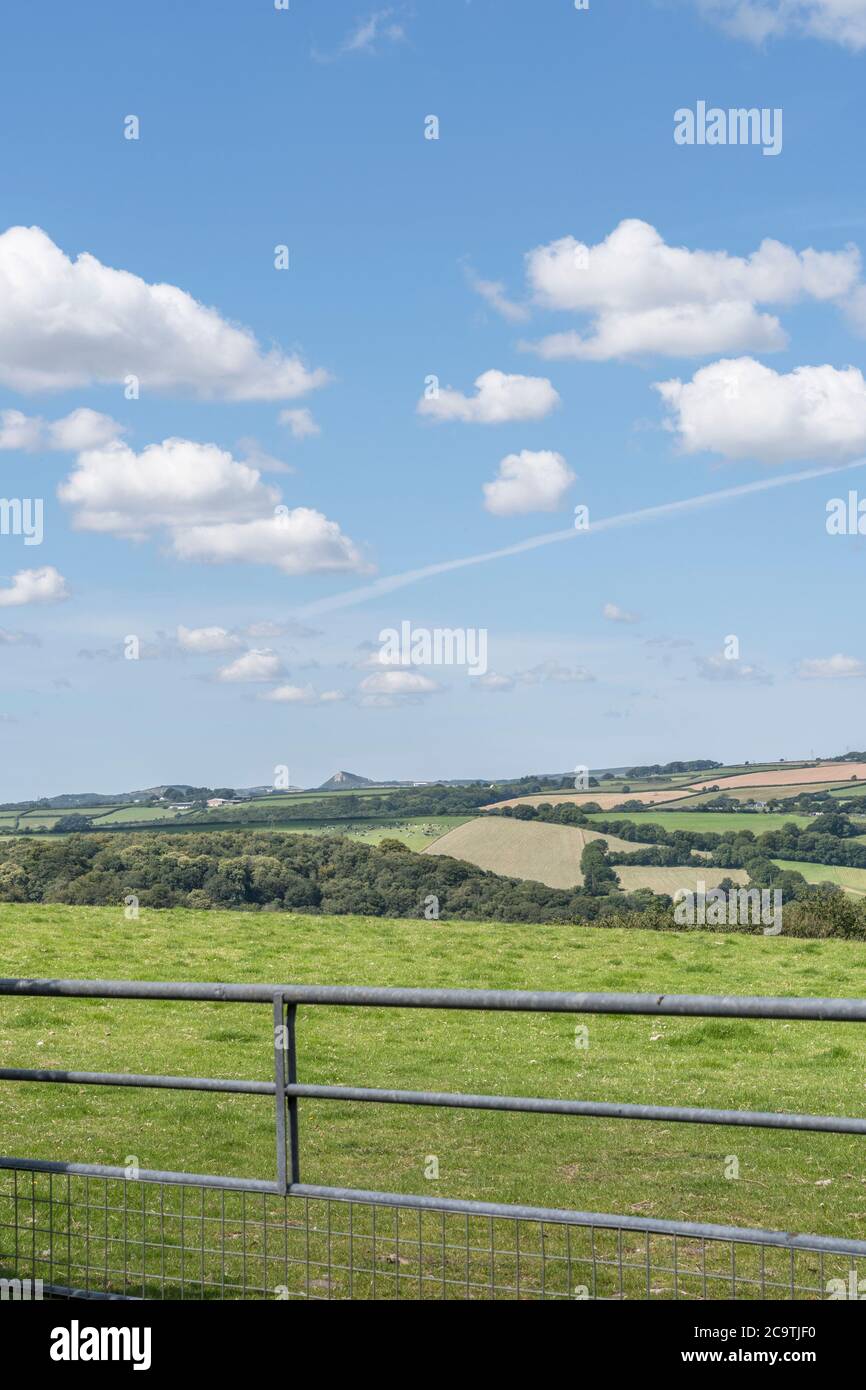 Fluffy cloud formation in blue sky over distant hillside field / farmland in UK, looking toward distant China Clay mining spoil heap on horizon. Stock Photo