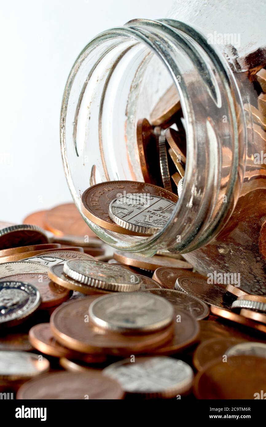 Close up still life of the open end of a coin jar on its side, the small denomination UK coins having spilled out. Concept of dipping into savings. Stock Photo