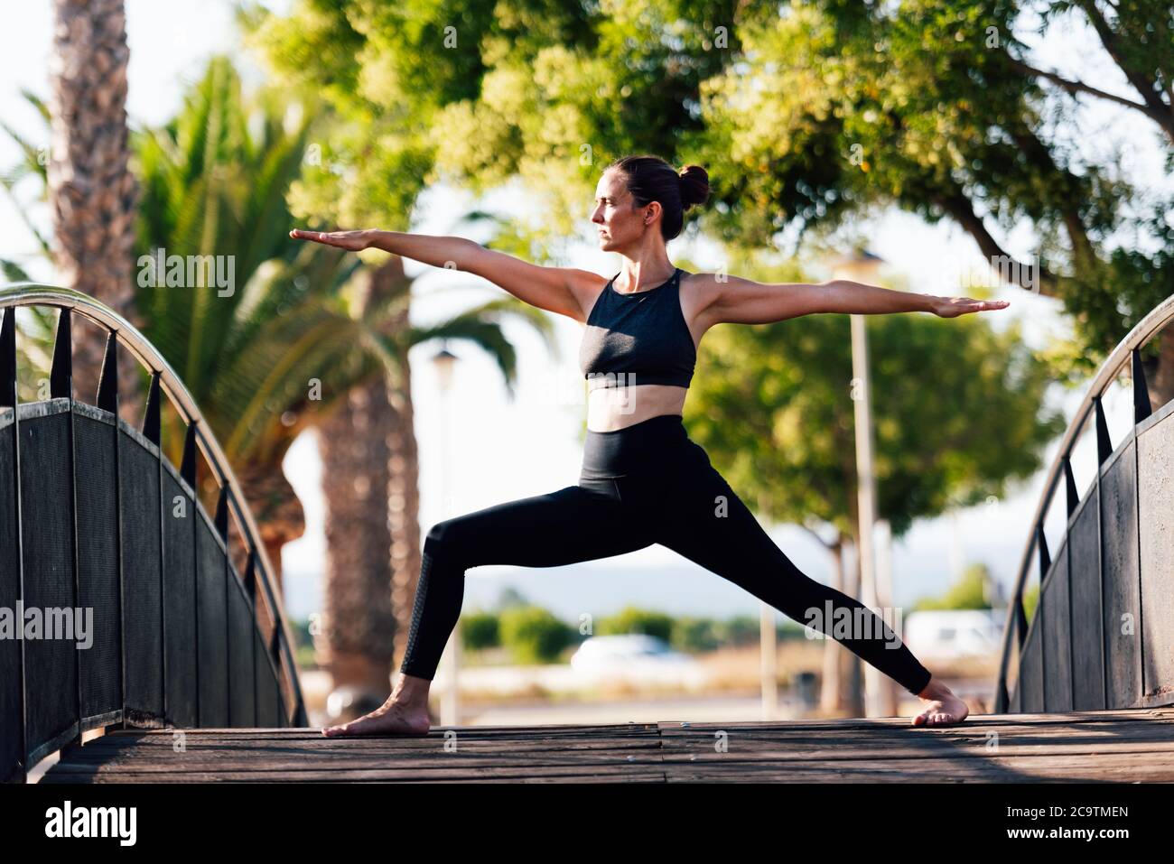 young woman doing exercises on outdoor copper wooden bridge surrounded by gardens Stock Photo