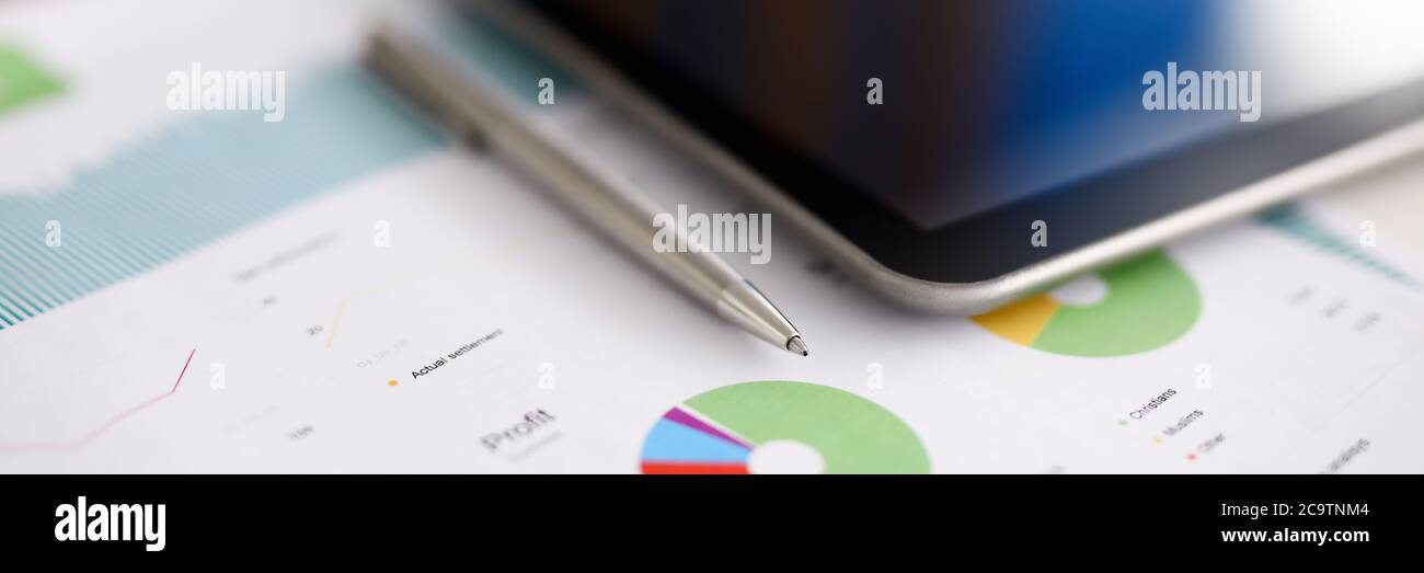 Silver pen adn digital tablet pc lie on office table against business chart background closeup Stock Photo